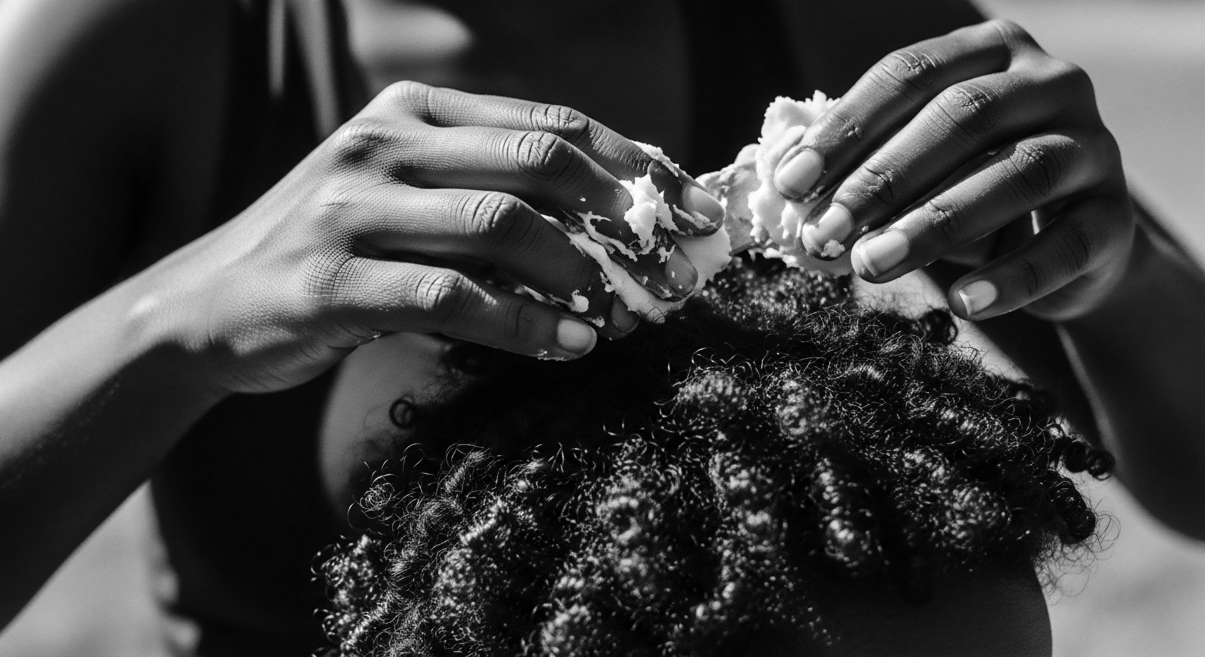 Applying Hair Cream to Coiled Hair: A Black and White Portrait The image celebrates the intimate act of nurturing textured hair, using rich ingredients on densely coiled strands, reflecting a commitment to holistic wellness and Black hair traditions. This ritual links generations through ancestral knowledge and the practice of self-love embodied in natural hair care.