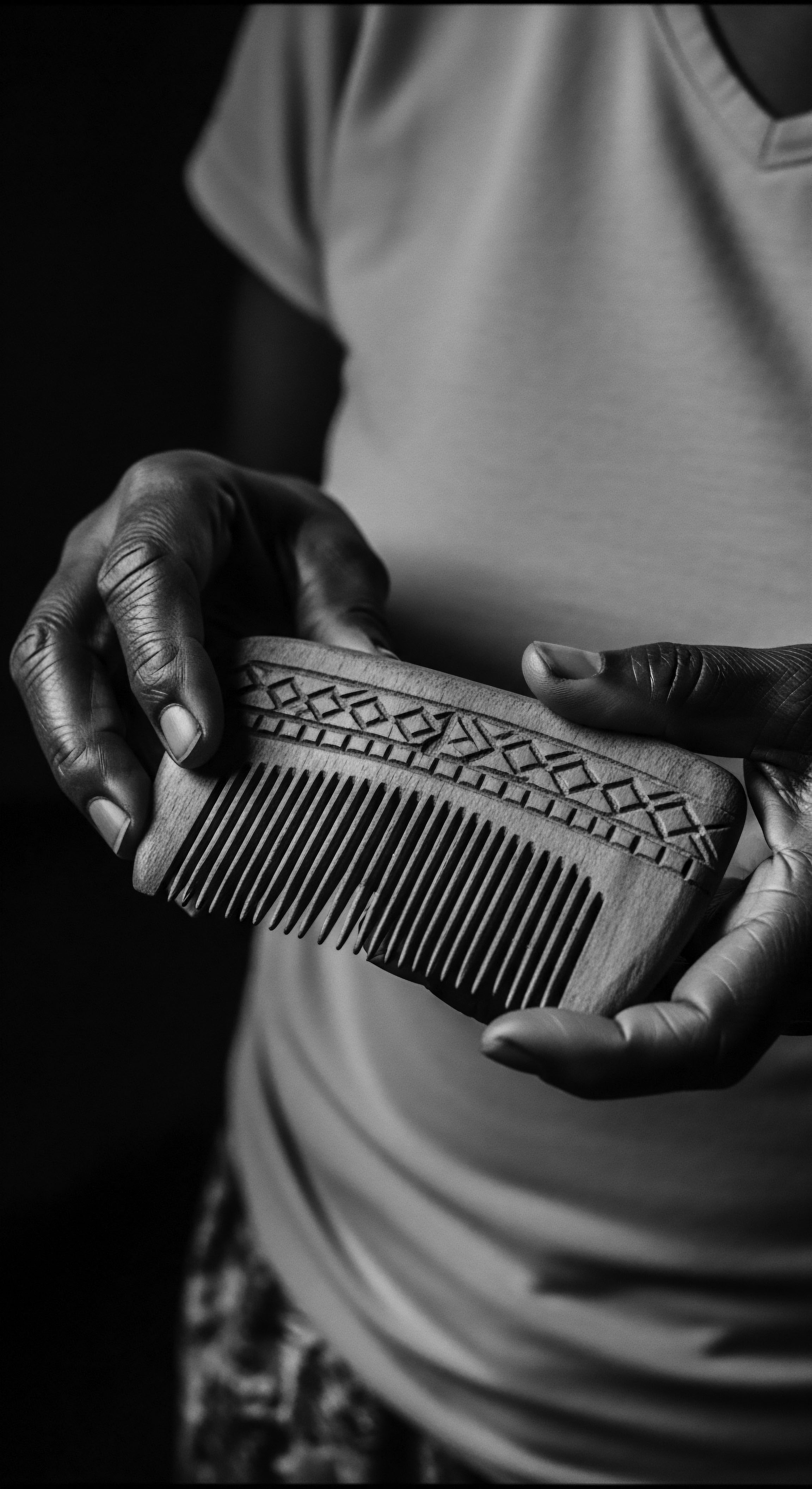 Artisanal Wooden Comb Held By Hand Displaying Rich Textural Heritage Echoing generations of ancestral heritage, the craftsman's wooden comb is held with care, a testament to the art of mindful grooming. Its geometric design speaks to expressive styling, weaving a rich narrative of wellness and authentic, holistic hair care for textured hair.