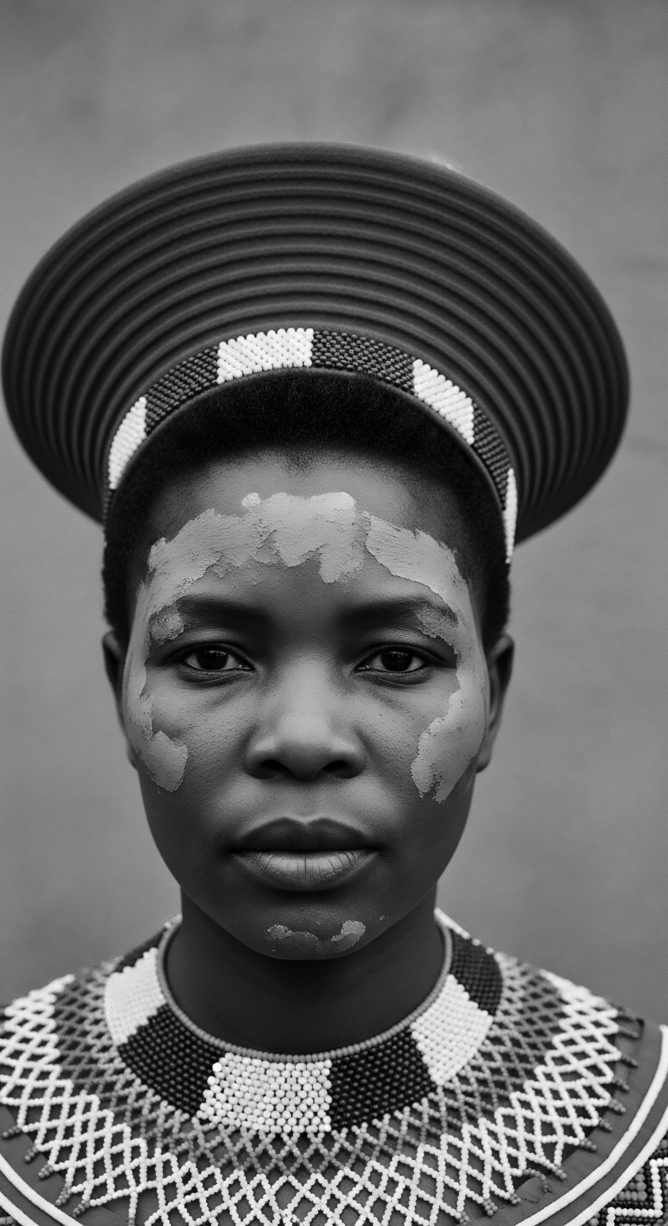 Black and White Portrait of a Woman Adorned in Traditional Headdress The portrait encapsulates a moment of cultural pride, expressed through traditional attire and facial markings. Her gaze meets the viewer's, inviting reflection on ancestral identity and the enduring beauty of textured hair within the context of cultural heritage.