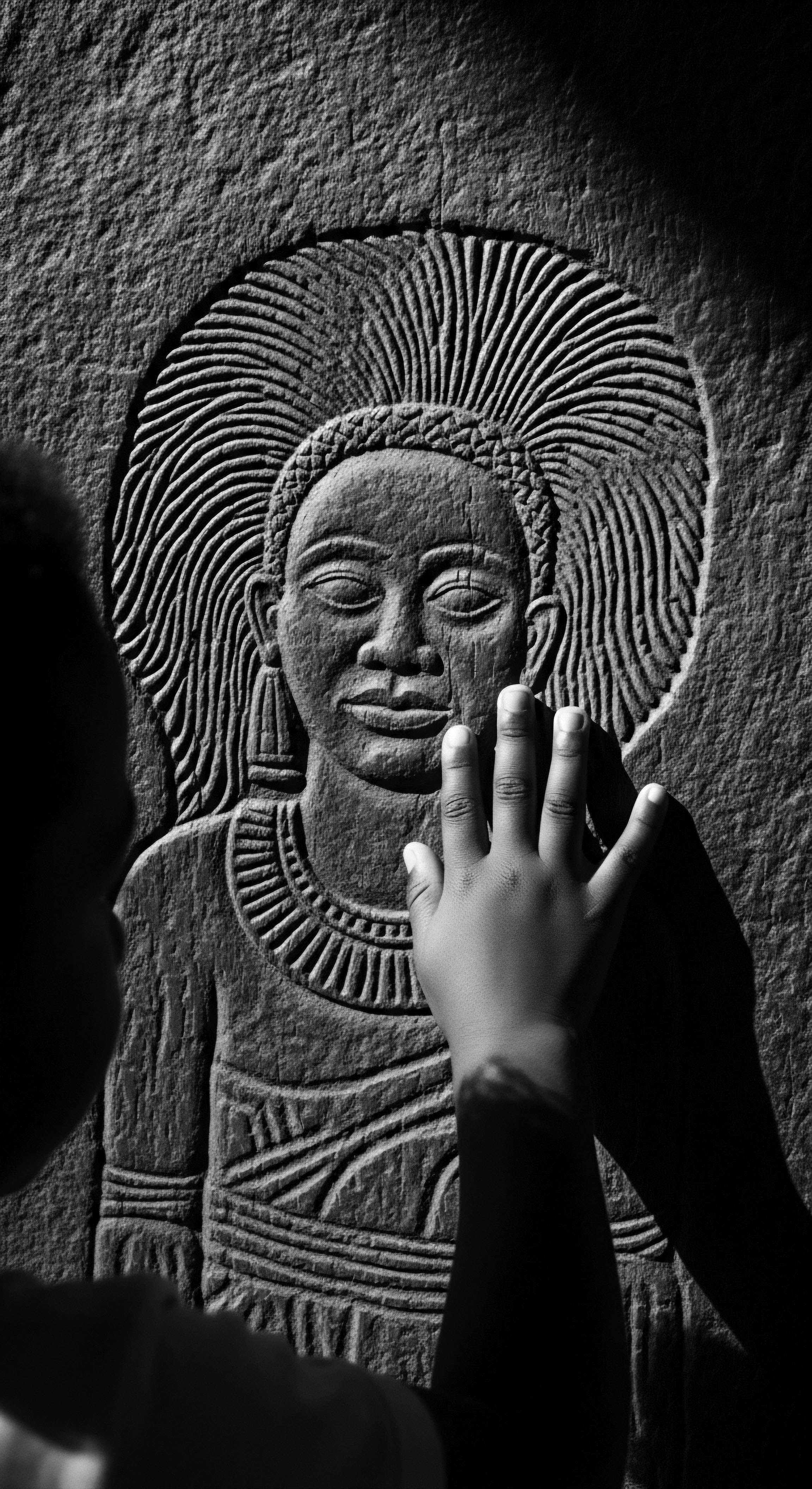 A child's touch bridges generations as they explore an ancient carving, feeling the depth and detail of a woman's textured hair representation, fostering a sense of connection to ancestral heritage and the enduring legacy of natural hair formations in art and cultural identity.