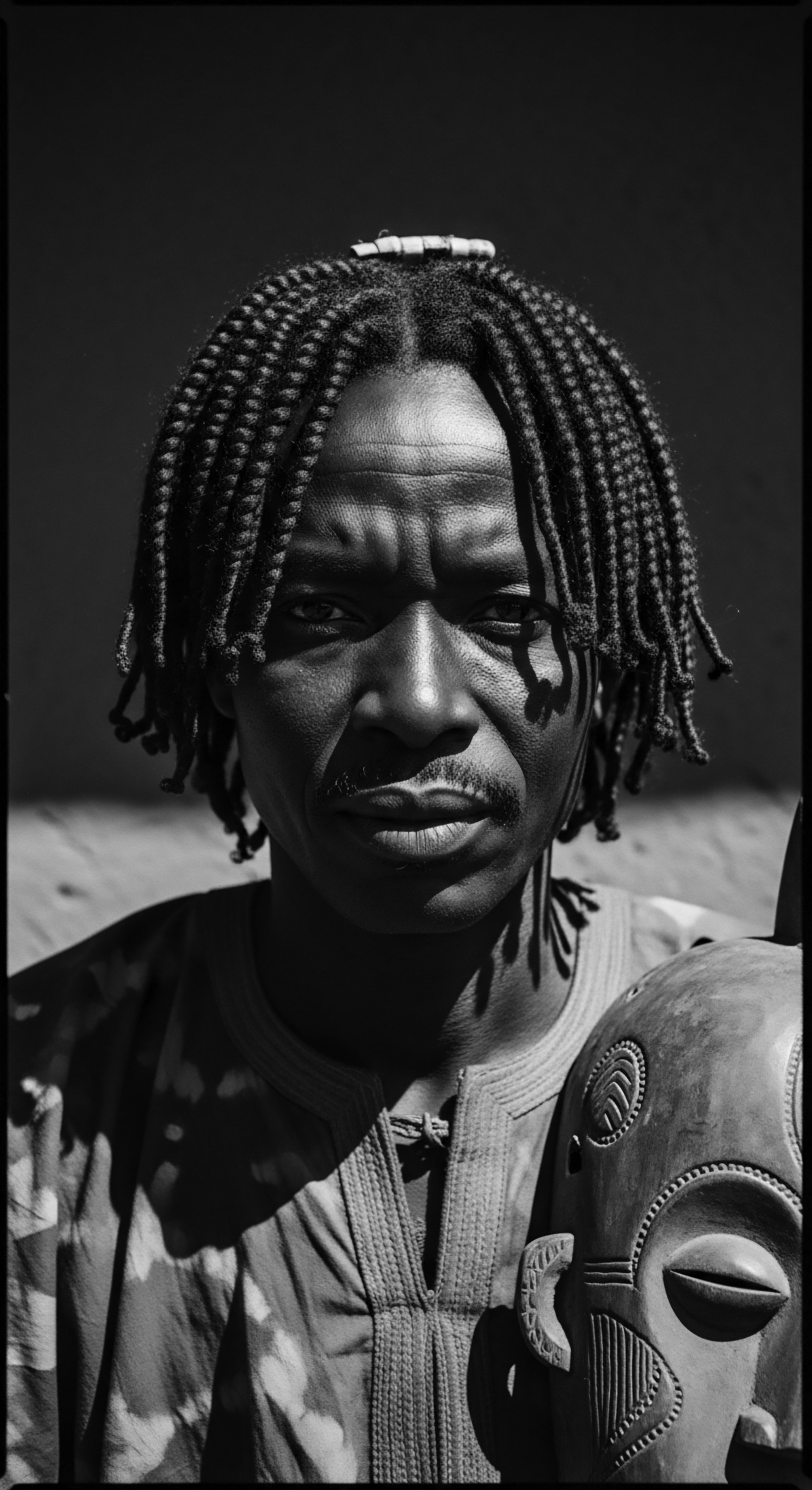 Dogon Man’s Striking Portrait With Traditional Mask and Braided Hair The Dogon man’s intense gaze and carefully braided hair, combined with the traditional mask, create a powerful visual narrative on heritage and identity. Textured hair patterns add visual depth and resonate with holistic hair care principles and styling practices in diverse mixed-race contexts.