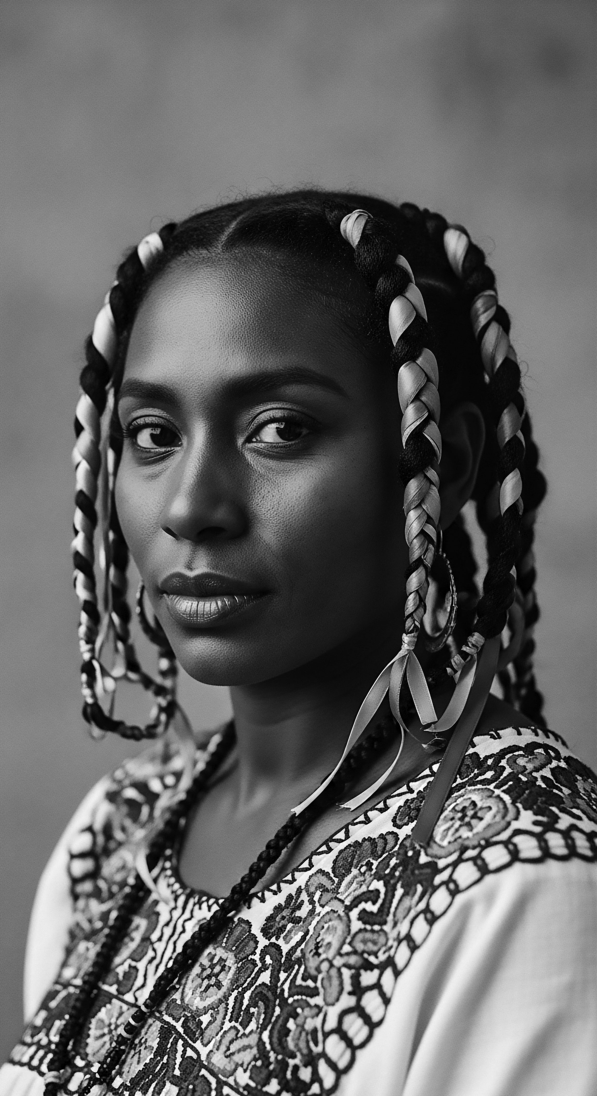 Elegant Portrait Black Woman Braids Accented with Ribbon Heritage Inspired Look The striking portrait explores ancestral beauty through her carefully styled braids, highlighting the cultural significance woven into her textured hair, which is complemented by her patterned traditional attire. The image invites contemplation on beauty standards, cultural representation, and mindful hair practice within heritage.