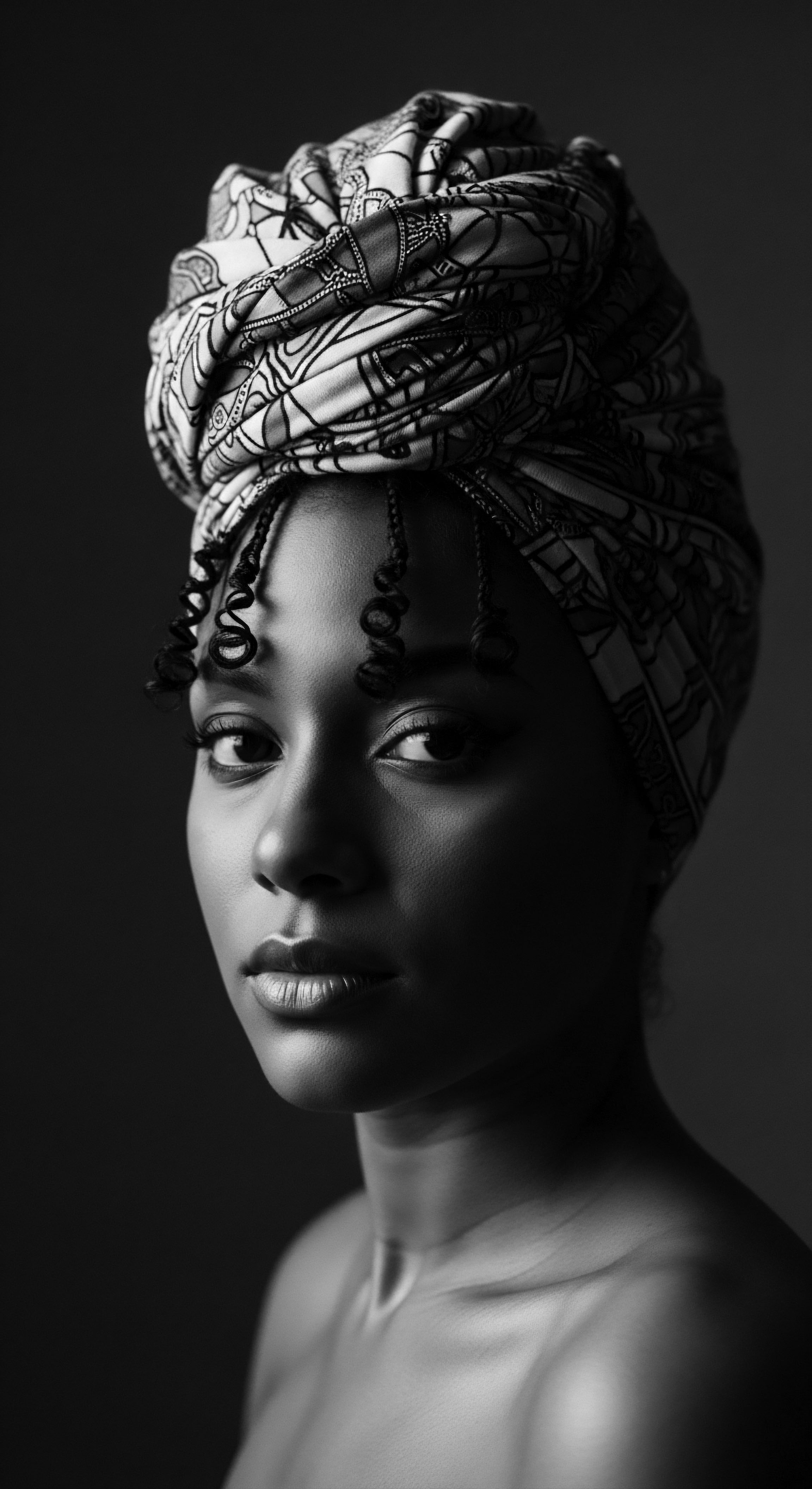 Elegant Portrait of Woman with Textured Hair Wrapped in Patterned Headwrap The monochrome portrait evokes timeless grace, showcasing the beauty of natural coiled texture and the artistry of a traditional headwrap. This image serves as an intimate exploration of self-expression, honoring ancestral heritage and the enduring power of cultural adornment, reflective of holistic self-care.