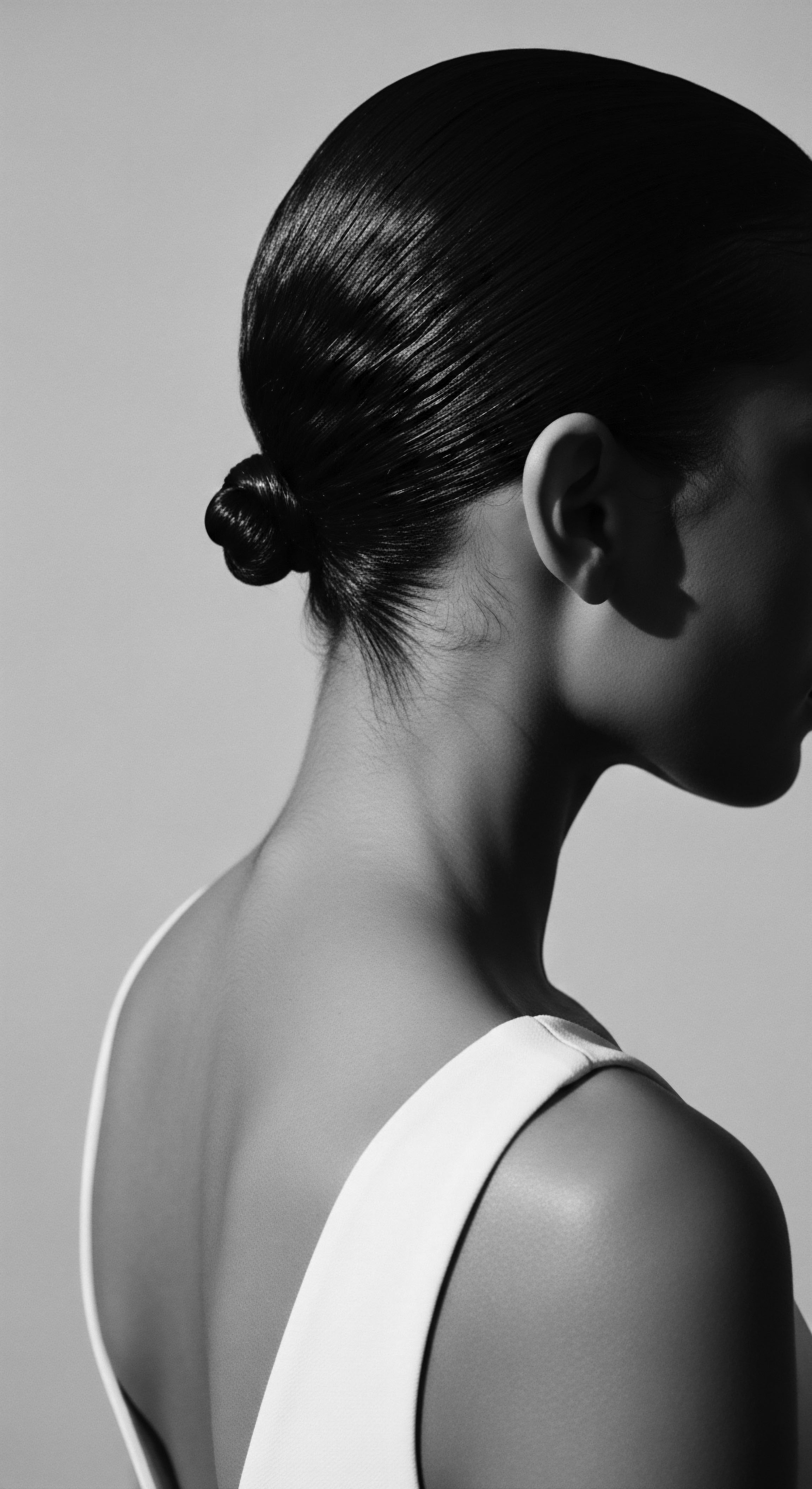 Elegant Updo Hairstyle Showing Fine Hair Texture and Nape of Neck Monochromatic artistic portrait showcases the elegant simplicity of a coiled updo hairstyle, drawing attention to the natural texture and form. Lighting highlights the smooth surface and creates a serene, classic aesthetic, while the backdrop emphasizes the clean, refined nature.