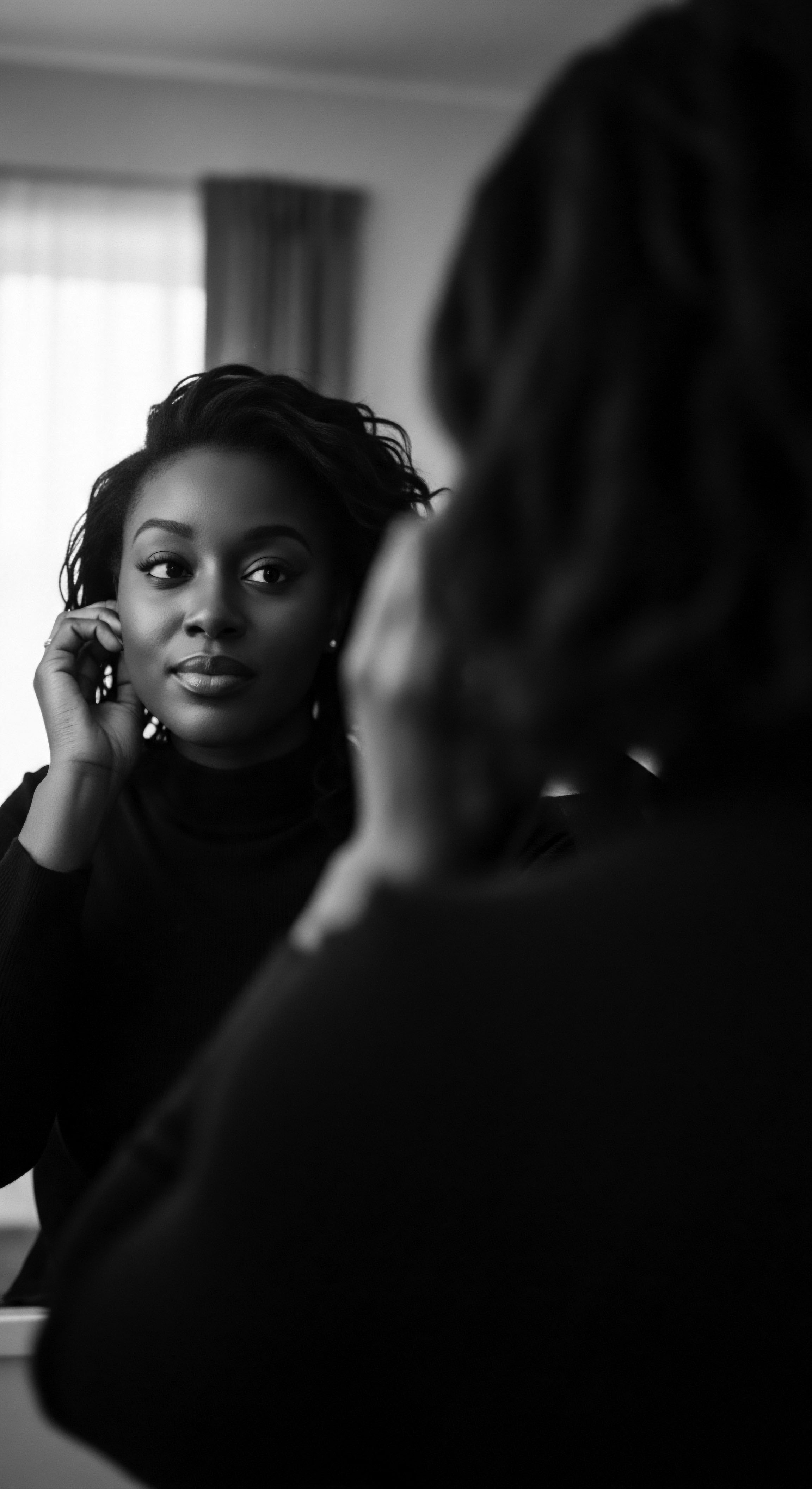 Elegant Woman Adjusting Earring Reflection Textured Hair Introspection Black and White The mirror reflects more than an image it captures a private moment of self-adornment, showcasing textured hair's intrinsic beauty in monochrome this scene speaks to a heritage of self-love, where personal style and reflection merge to celebrate the expressive and empowering facets of identity, style.