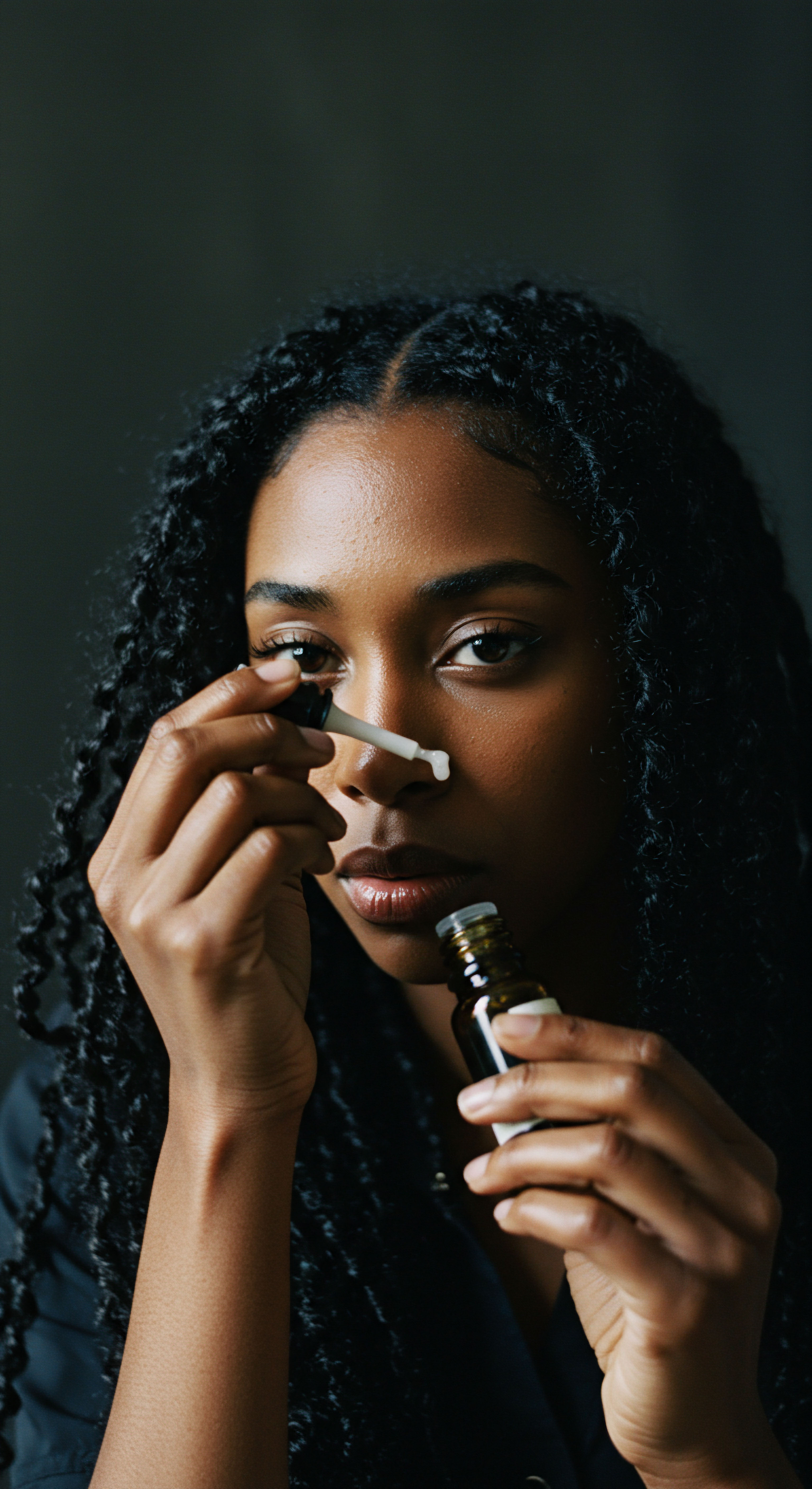 Empowering Textured Hair Wellness Journey Daily Hydration Ritual Celebrating self-care, a Black woman applies a restorative serum, accentuating her radiant melanin-rich complexion. Her luscious high-density micro-coils signify ancestral heritage and deep moisture retention. This illustrates a mindful daily regimen focused on epidermal hydration and comprehensive scalp health for achieving vibrant, resilient hair fibers.