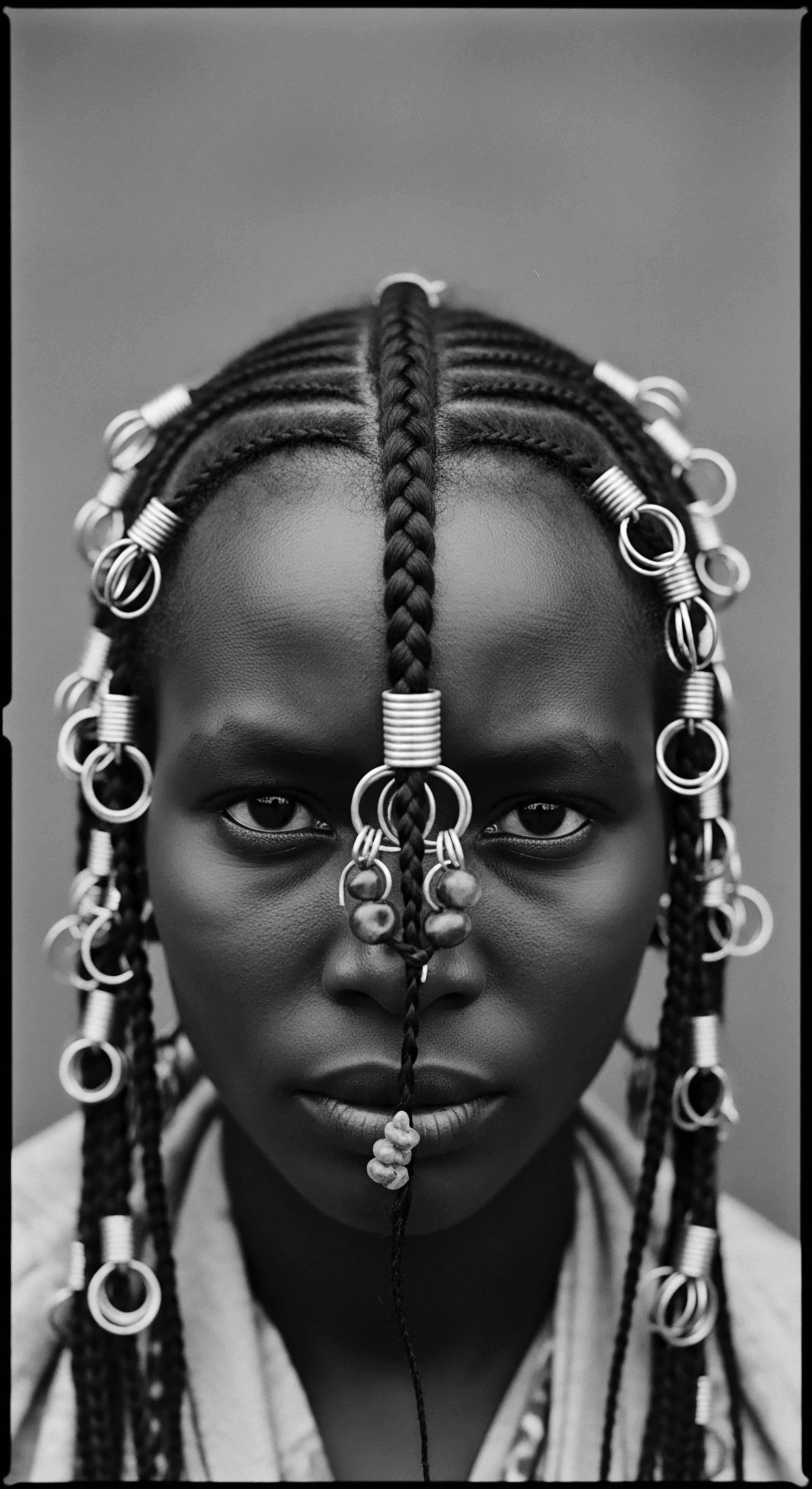 Fulani Braiding Artistry Silver Adornments Youthful Gaze Black and White Portraiture This striking Fulani braiding artistry embodies ancestral pride, showcasing the integration of silver adornments as symbols of identity, reflecting a commitment to holistic hair care while highlighting sebaceous balance care as integral to the health and expression of textured coils.