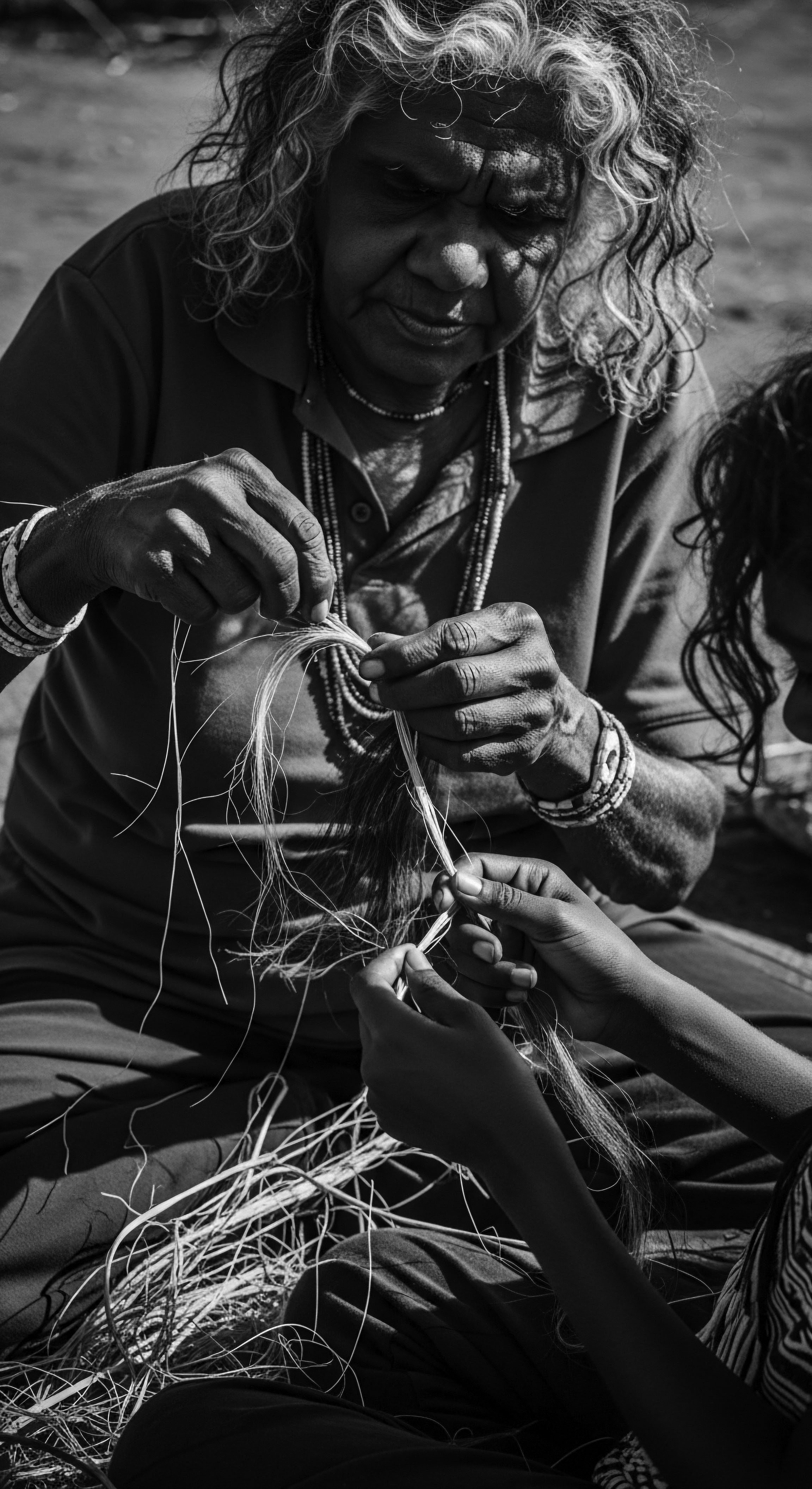 Intergenerational Kinship Weaving Wisdom Textured Hair Legacy in Black and White Resilient hands, embodying ancestral heritage, pass down the art of fiber work, reflecting shared wisdom through textured hair kinship. The monochrome palette accentuates depth, emphasizing holistic connection and the transference of cultural identity woven into each fiber, highlighting timeless Black hair traditions.