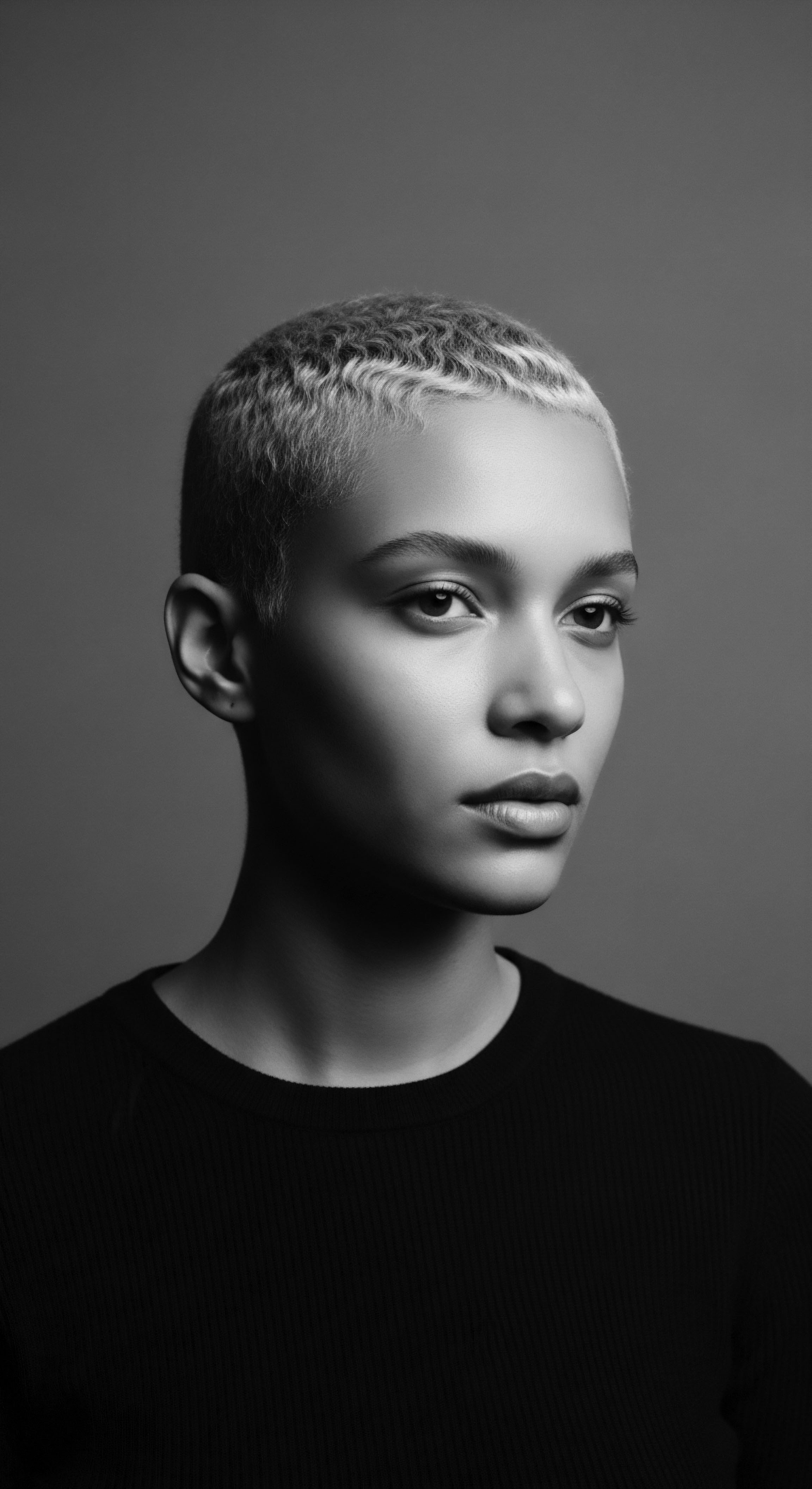 Monochromatic Portrait of a Woman With Short Natural Blonde Coiled Hair This portrait's sharp contrast and nuanced lighting draws the eye to the subject's beautifully short coiled hair, a testament to individual expression and the embracing of natural textures. It celebrates a contemporary aesthetic rooted in heritage, resilience, and holistic self-acceptance within mixed-race hair narratives.