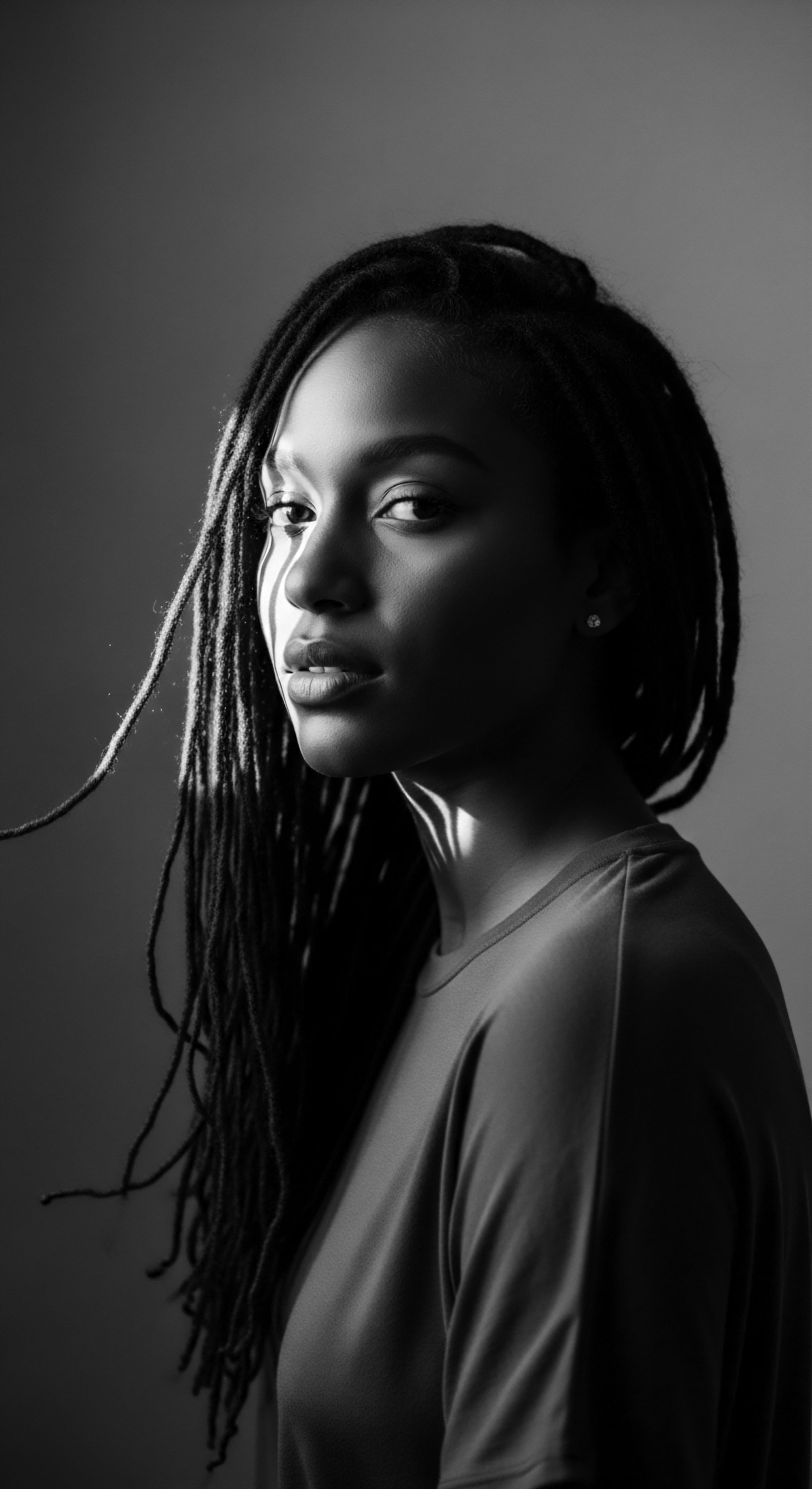 Monochromatic Portrait of an African American Woman with Locs and Shadow Play This evocative portrait of a woman adorned with locs captures the interplay of light and shadow, accentuating both strength and vulnerability. The image honors the heritage of textured hair while inviting viewers to contemplate the complexities of identity, beauty standards, and the ongoing dialogue around hair expression.