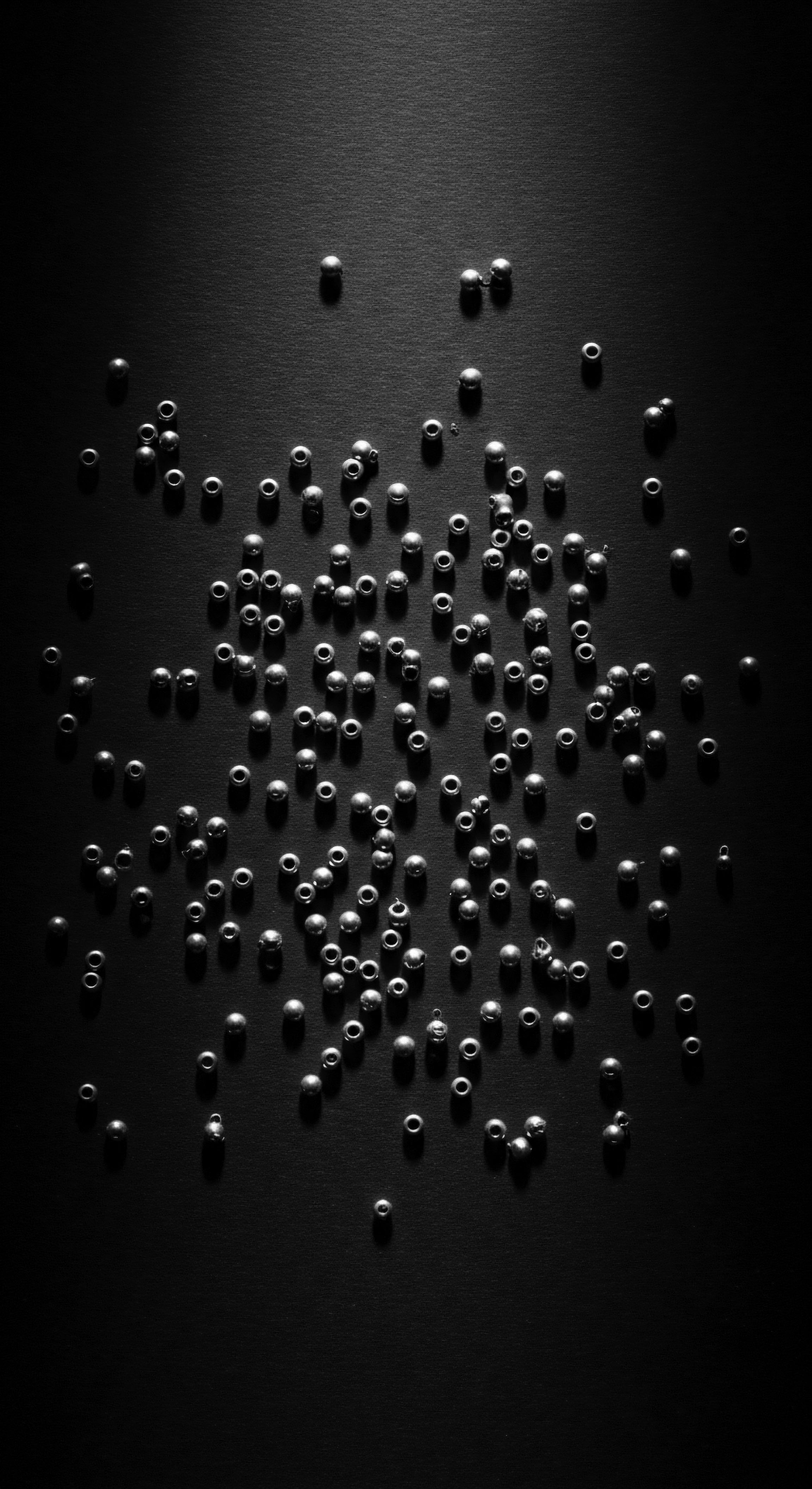 A monochrome studio image displays a scattering of small, spherical beads across a black surface. Precise lighting emphasizes shadows, bringing depth to the composition. The interplay highlights holistic wellness, and natural elements central to many textured hair heritage practices. Ancestral wisdom echoes in simplicity.