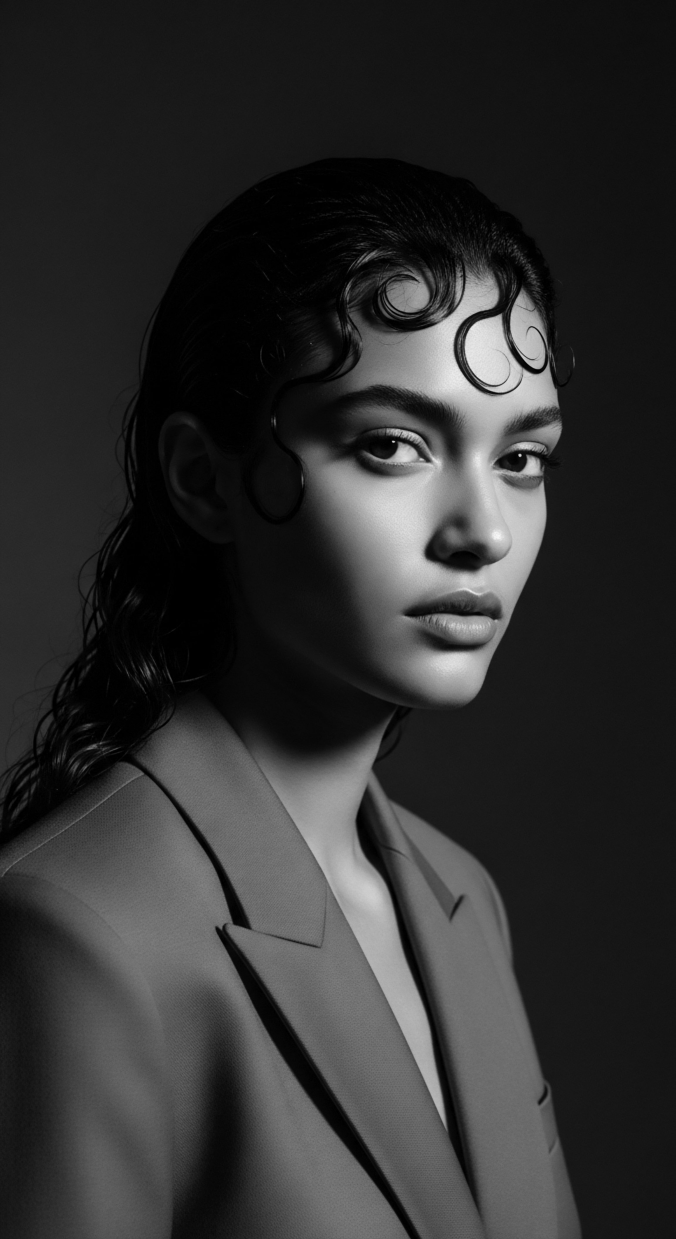 A stunning monochrome portrait reveals a woman with meticulously styled wet textured hair finger waves cascade across her forehead, a testament to heritage hairstyling. The soft light sculpts her face, casting subtle shadows accentuating her poise and the intricate wave patterns, reflecting timeless elegance and ancestral connection.