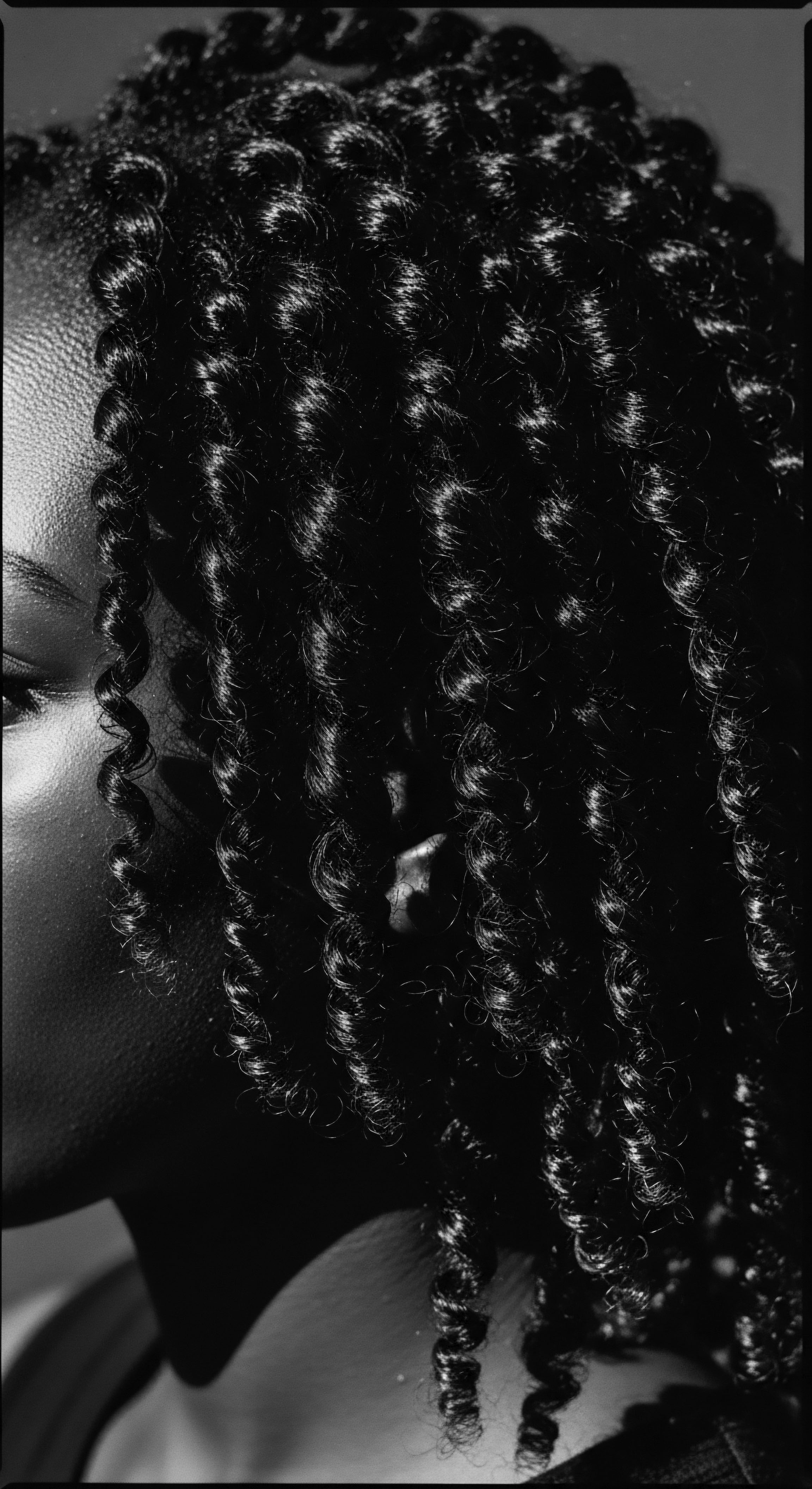 Monochrome Portrait Highlighting Textured Hair Coils and Radiant Skin Tone Intense contrasts in the monochrome shot bring forth the beauty of coiled textured hair formations, a testament to ancestral heritage. The artful play of light and shadow highlights skin's radiance and texture, invoking deep contemplation on wellness and identity through unique Black hair narratives.