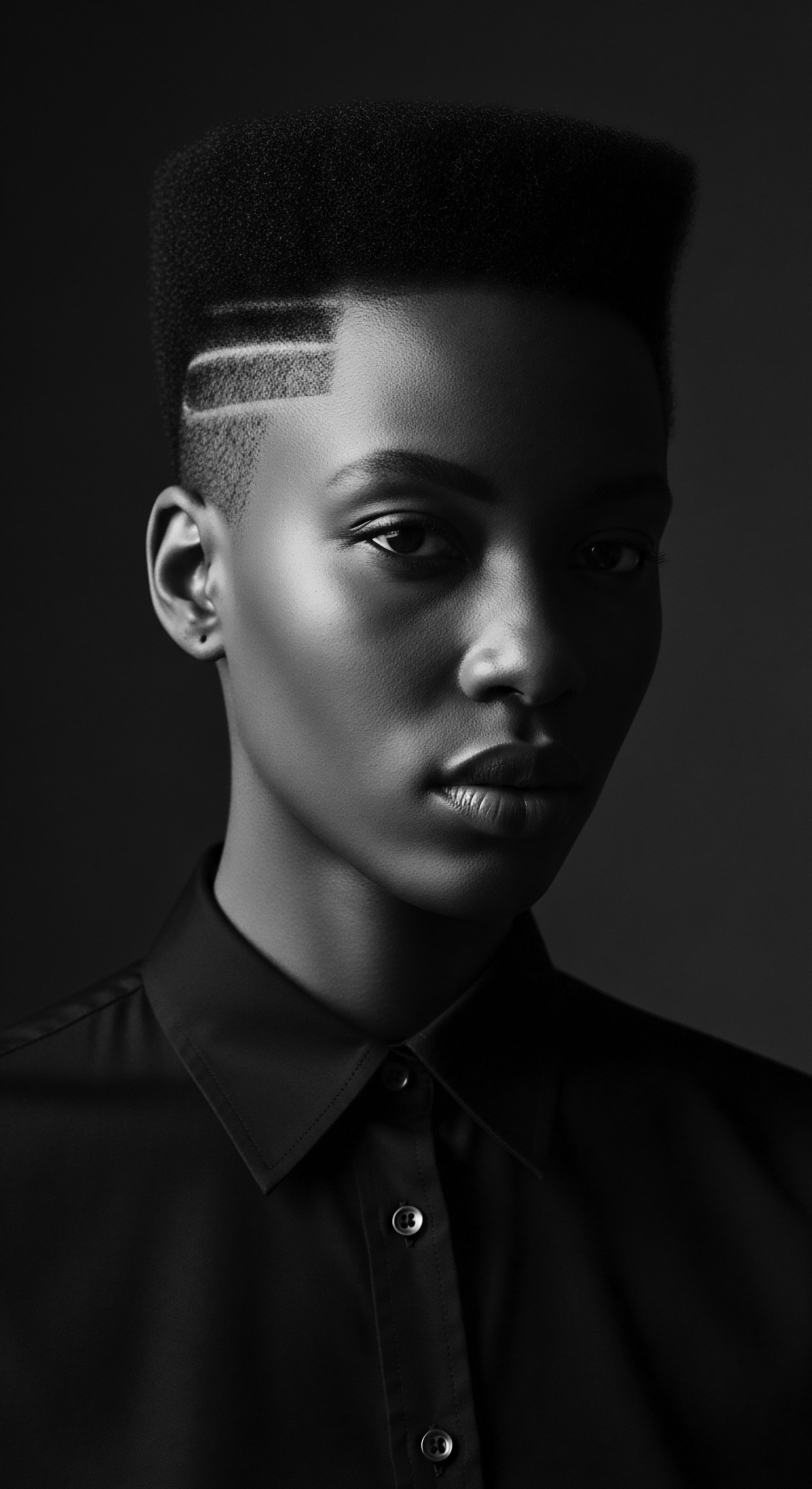 Monochrome Portrait of a Person with Coiled Textured Hair and Graphic Lines The monochrome artistry captures the essence of individuality, as graphic lines accentuate the short, dark, coiled texture of hair, presenting a modern style deeply rooted in cultural expression. The portrait echoes strength, identity, and the intentionality behind self-representation through distinct hair styling.