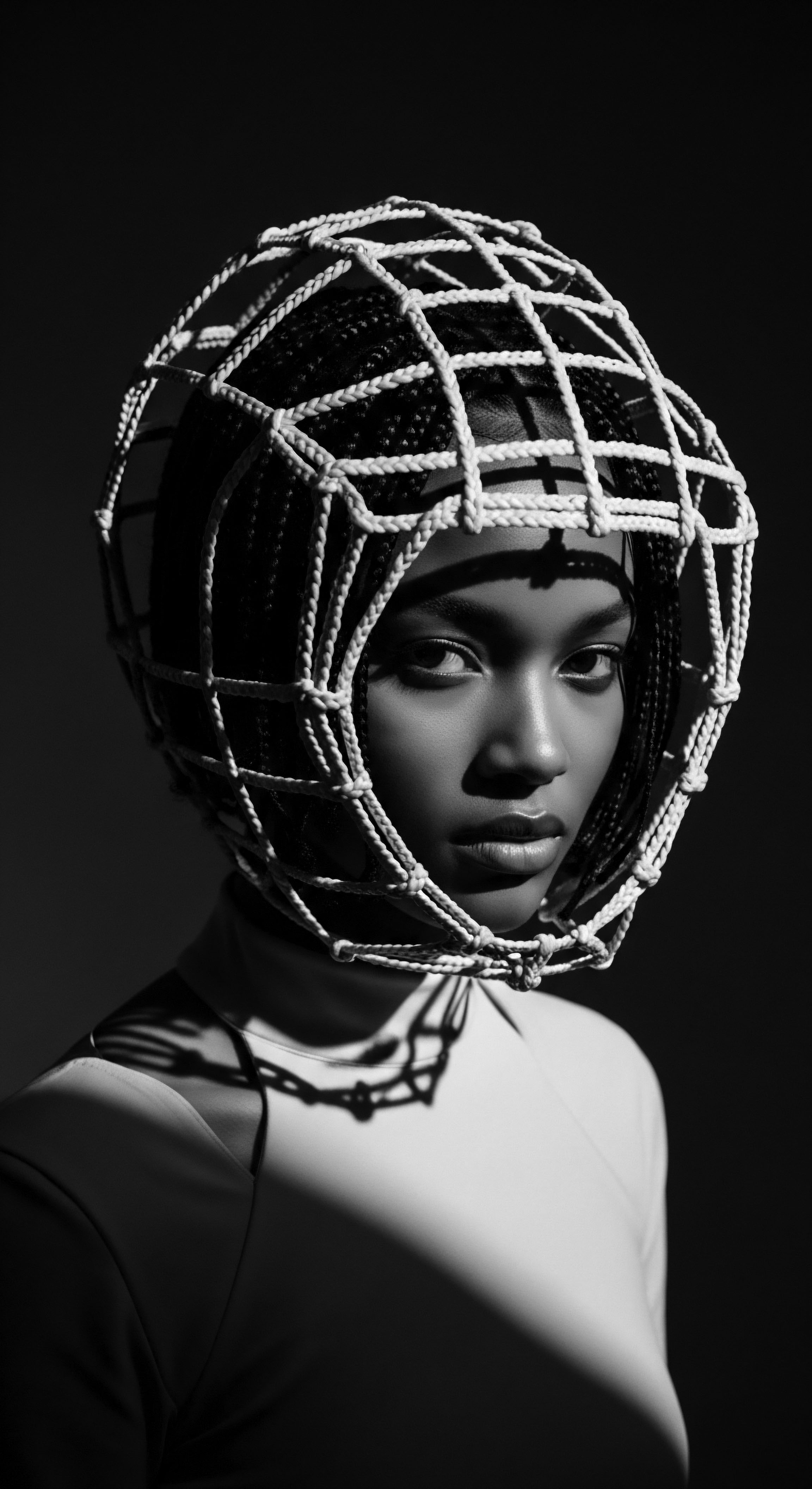 Monochrome Portrait of a Woman Wearing Artistic Braided Hair Cage The portrait evokes an exploration of identity framed by artistic constraints, where the rope cage symbolizes both protection and artistic expression. Intricate cornrows beneath the cage display Black hair traditions blending ancestral heritage with modern style enhancing natural textures through innovative braided artistry and thoughtful light use.