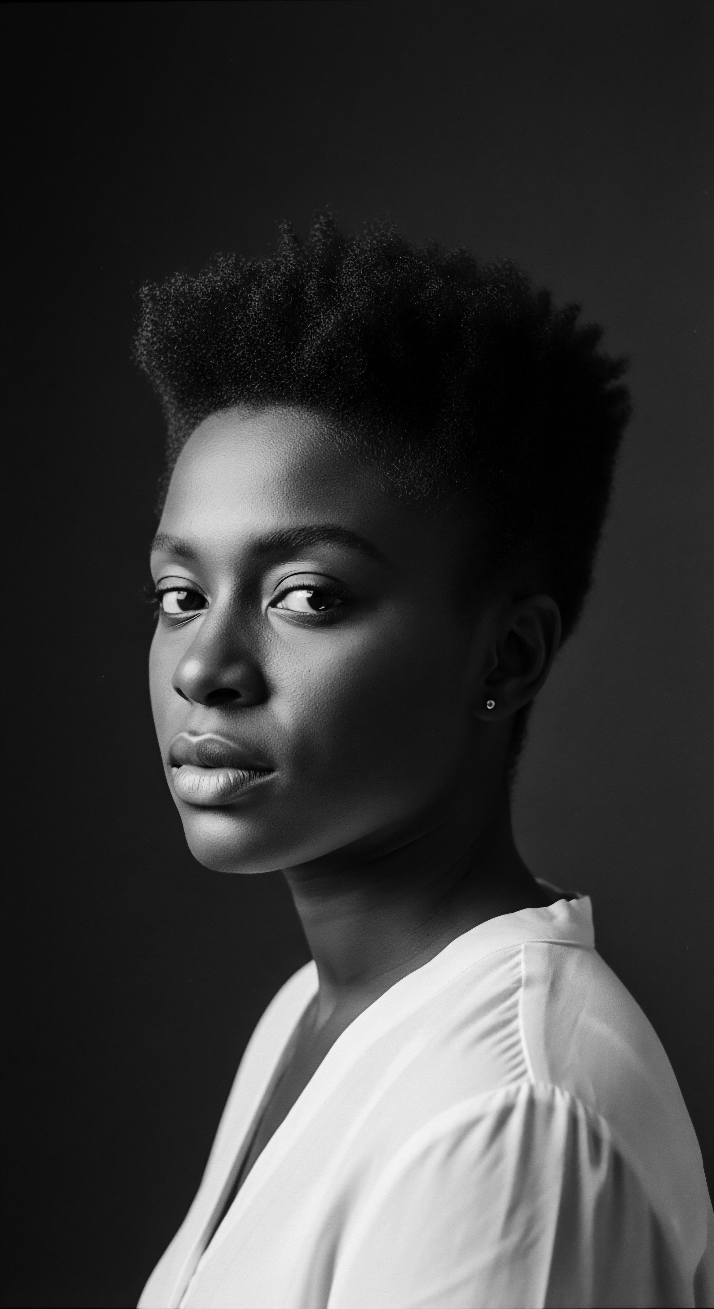 Monochrome Portrait of a Young Black Woman with Tightly Coiled Hair This monochrome study captures the grace and strength of a young Black woman, her tightly coiled hair a testament to natural beauty and cultural pride. The portrait's simplicity invites contemplation on heritage and identity, celebrated within a holistic embrace of natural hair care and expressive self representation.