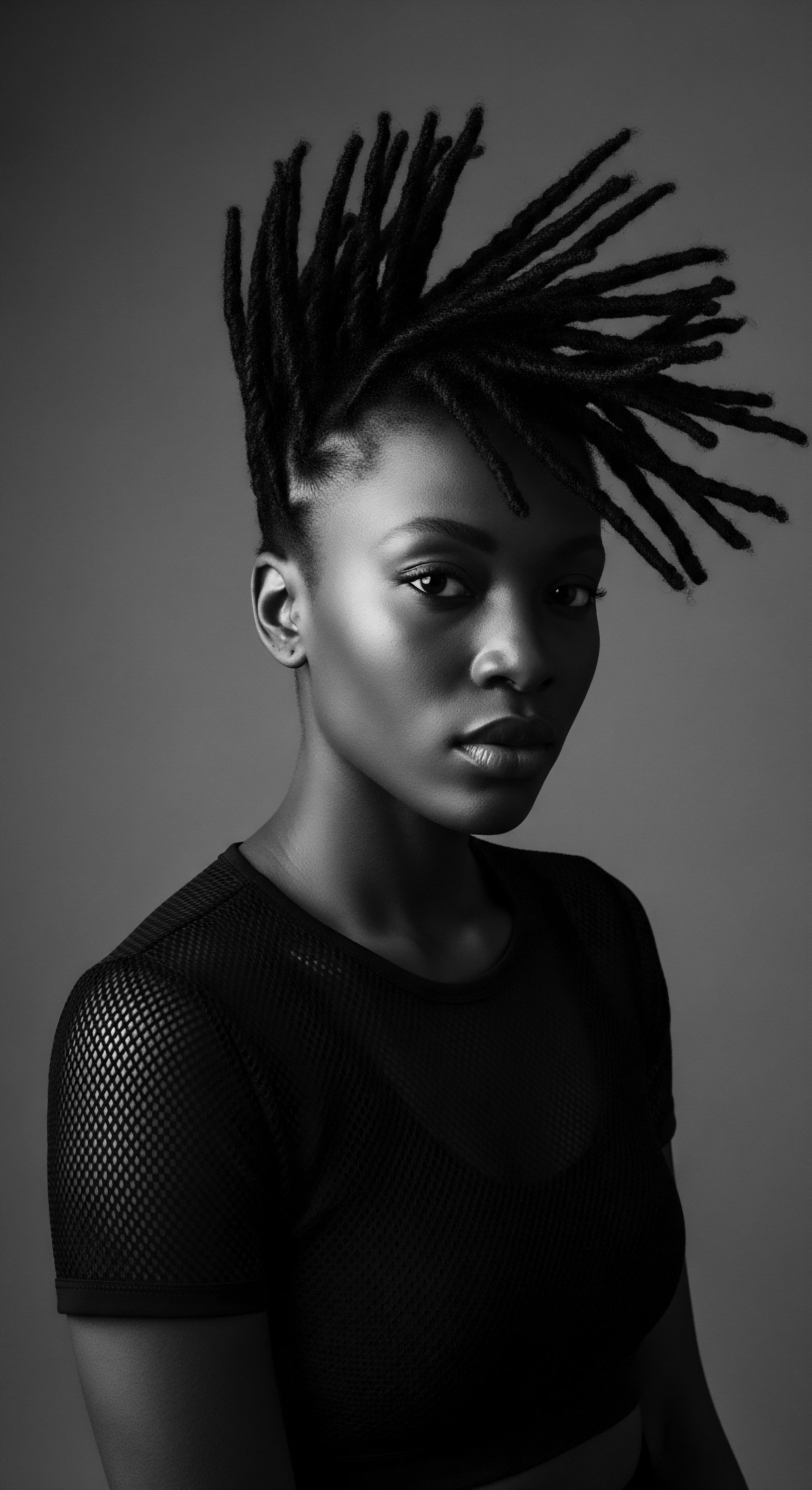 Monochrome Portrait of Black Woman with Styled Dreadlocks and Mesh Top This striking monochrome portrait celebrates the beauty and versatility of textured hair, particularly the intricate styling of dreadlocks, set against the striking contrast of light and shadow, inviting a deeper appreciation for modern Black hair artistry and cultural pride.