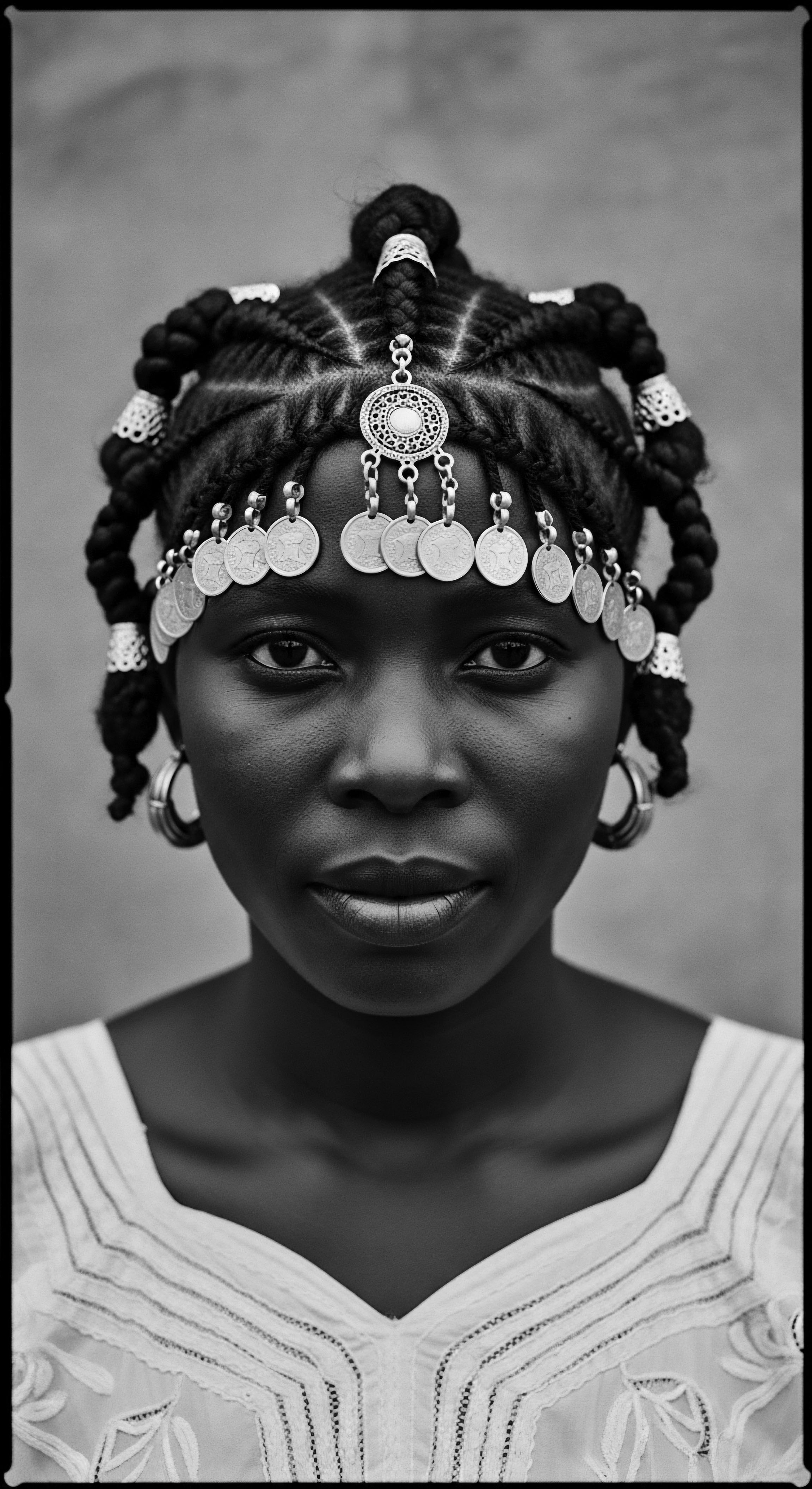 Monochrome Portrait of Woman Adorned with Braids and Coin Headdress Braided formations and coin ornamentation, captured in monochrome, reflect a legacy of self-expression. Cultural pride resonates through the detailed hair work, embodying wellness through ancestral hairstyles. The image's texture celebrates African heritage and natural beauty, amplified by the subject's poised gaze.