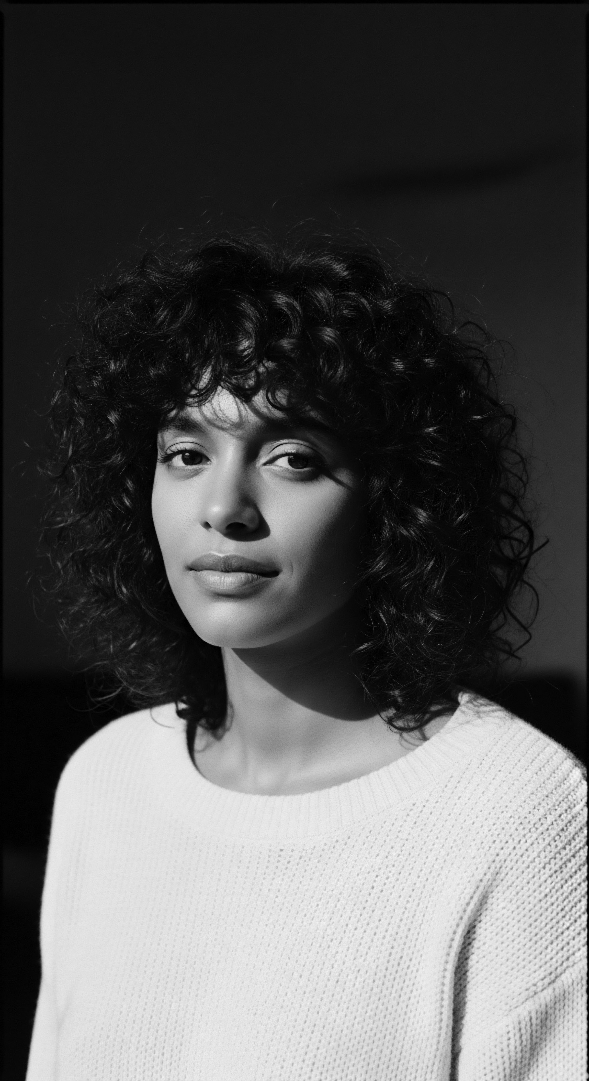 Monochrome Portrait of Woman with Naturally Coiled Hair in Sunlight Captured in monochrome, the subject's natural coiled hairstyle speaks volumes about embracing authentic beauty standards, cultural pride, and the conscious decision to move away from conventional norms. The portrait invites contemplation of the intersection between identity, ancestral heritage, and expressive styling reflected in her textured hair.