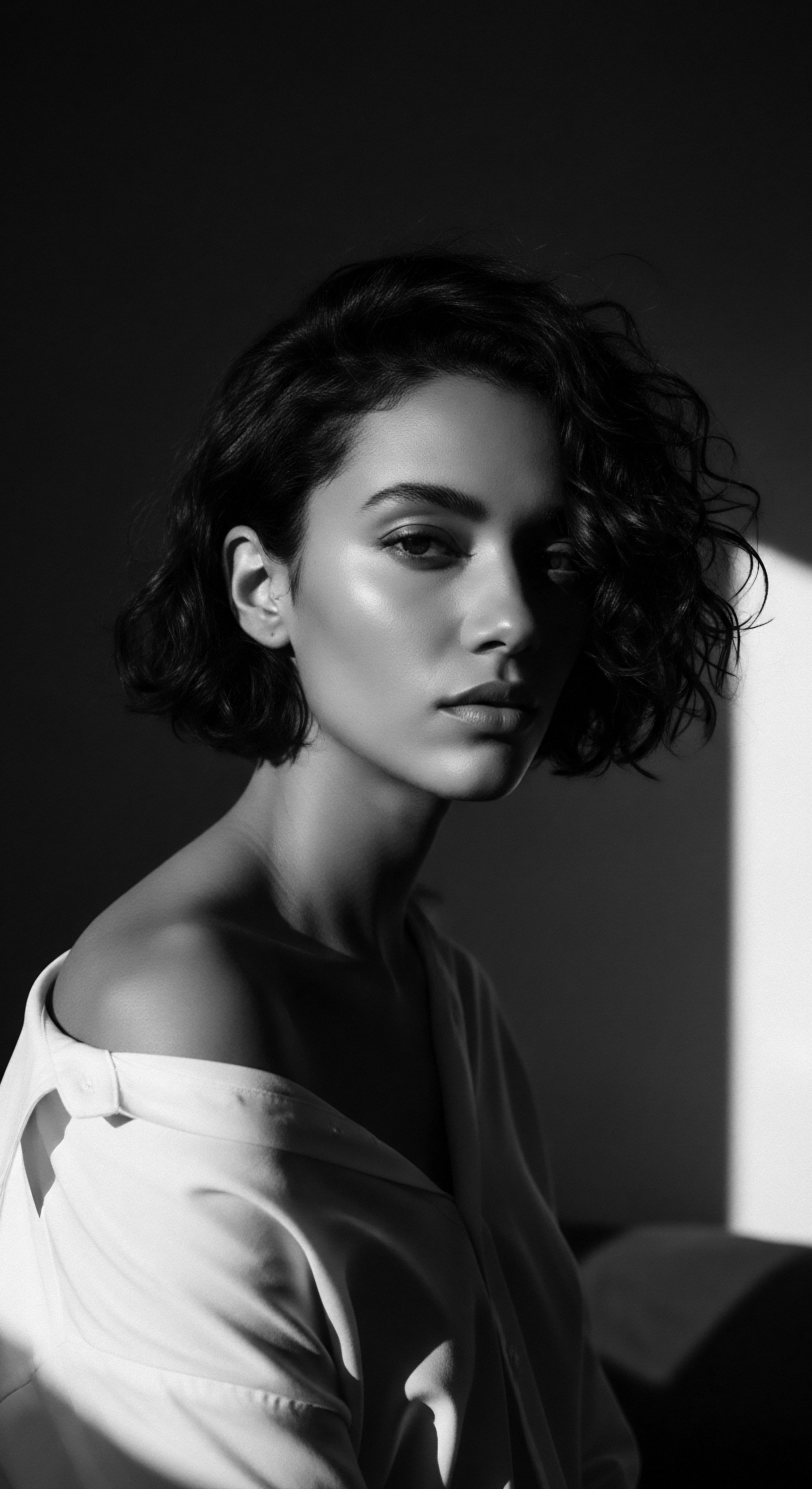 Monochrome Portrait Radiant Woman Short Coiled Hairstyle with Striking Shadow The monochrome portrait unveils the expressive potential of short, coiled textured hair, illuminated by dynamic shadows that accent the face. The image celebrates the confluence of ancestral heritage and modern styling techniques, highlighting the beauty and adaptability of natural mixed race textured hair.