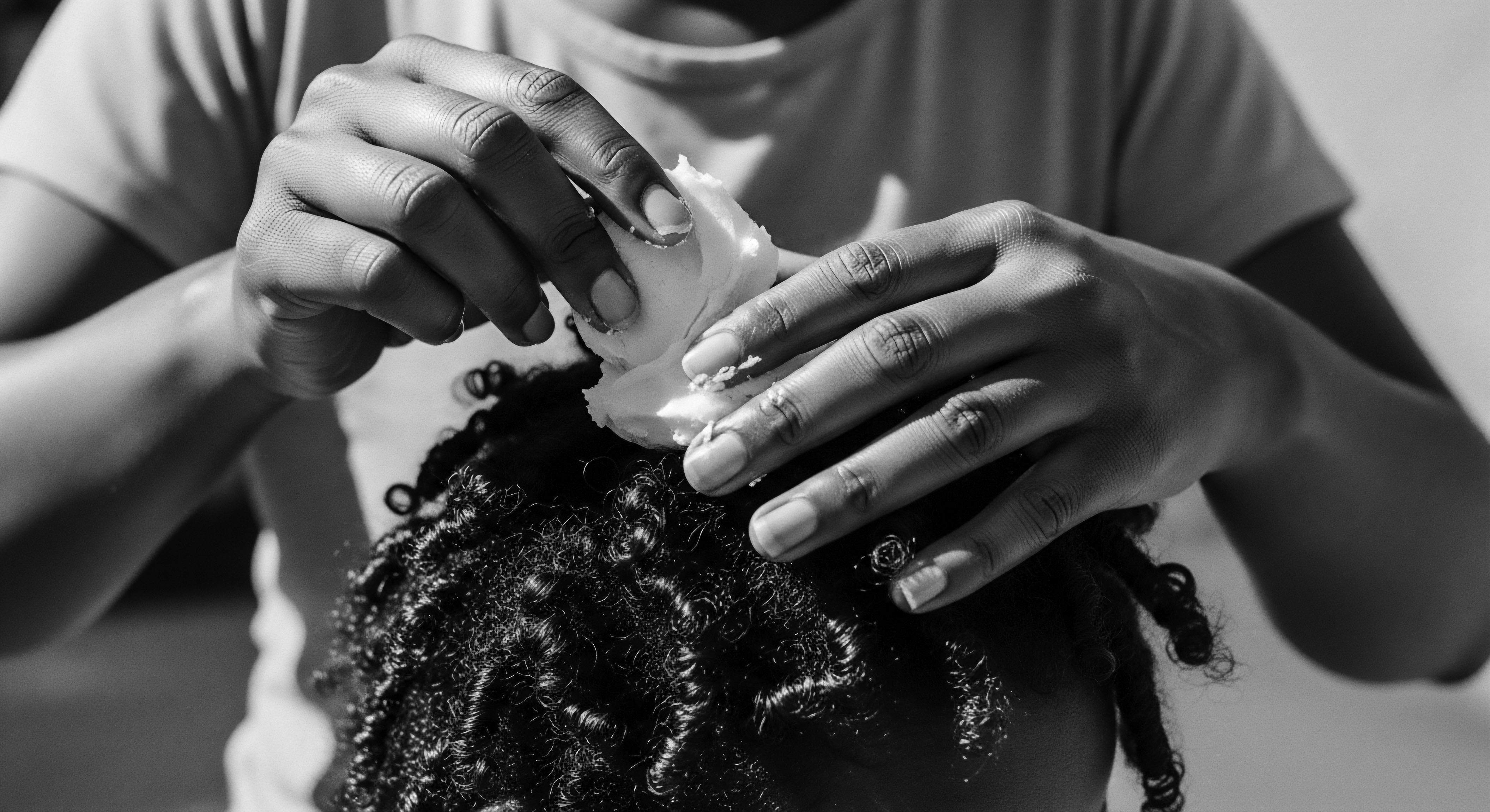 Nourishing Textured Hair Deep Moisture Treatment Application Black and White The image conveys a moment of intimate care, as hands apply a rich moisturizer to tightly coiled hair, celebrating the beauty and strength of Black hair traditions and holistic care. This act embodies cultural identity, ancestral connection, and wellness for expressive styling, nourishing the hair's natural resilience.