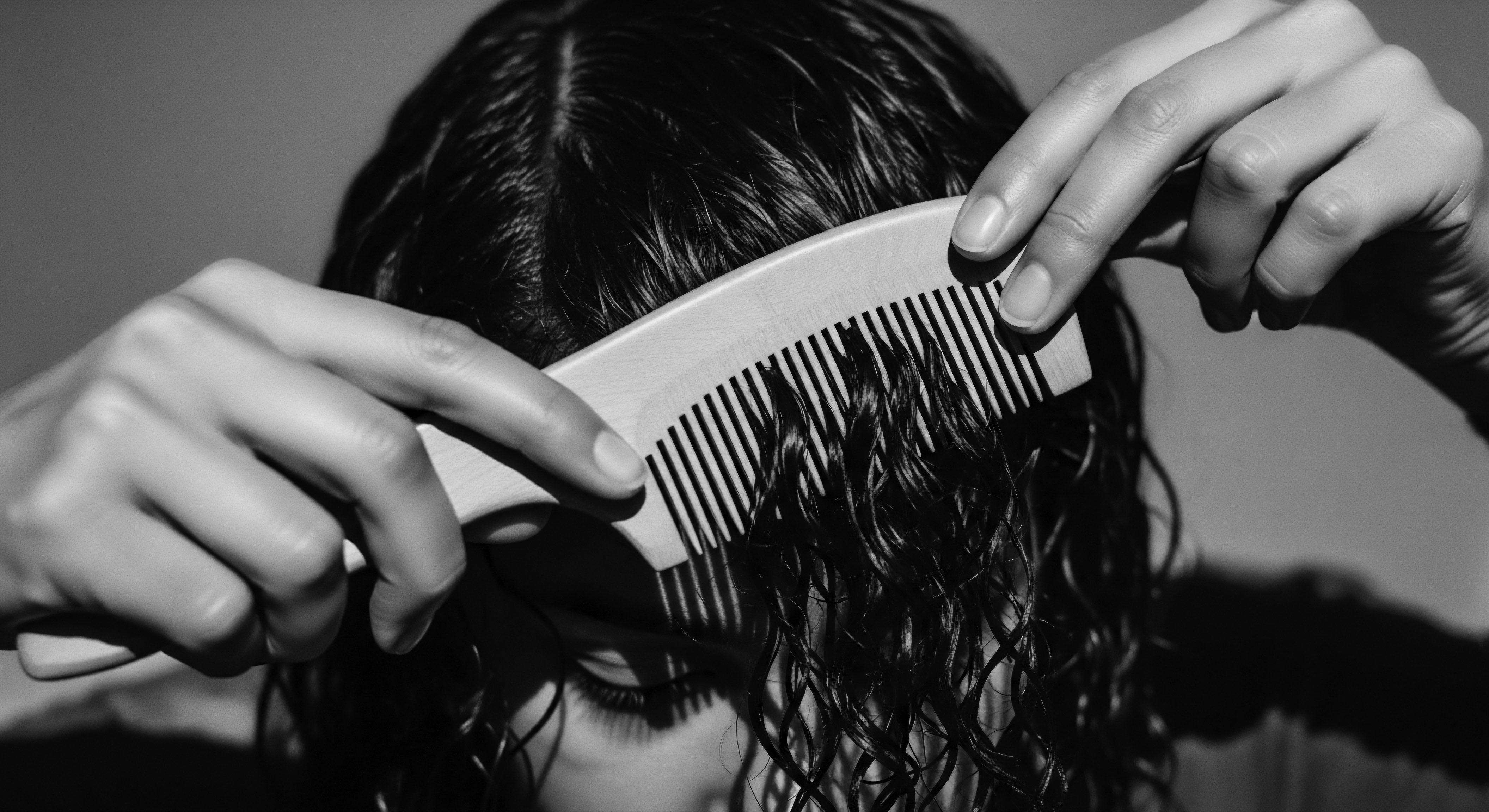 Person Combing Dark Coiled Hair with Wooden Wide Toothed Comb This intimate monochromatic image showcases a mindful approach to dark, coiled hair maintenance through controlled combing, symbolizing a deep connection to ancestral grooming traditions and the art of nurturing one's unique textured hair identity with simple yet effective practices like using quality care products.