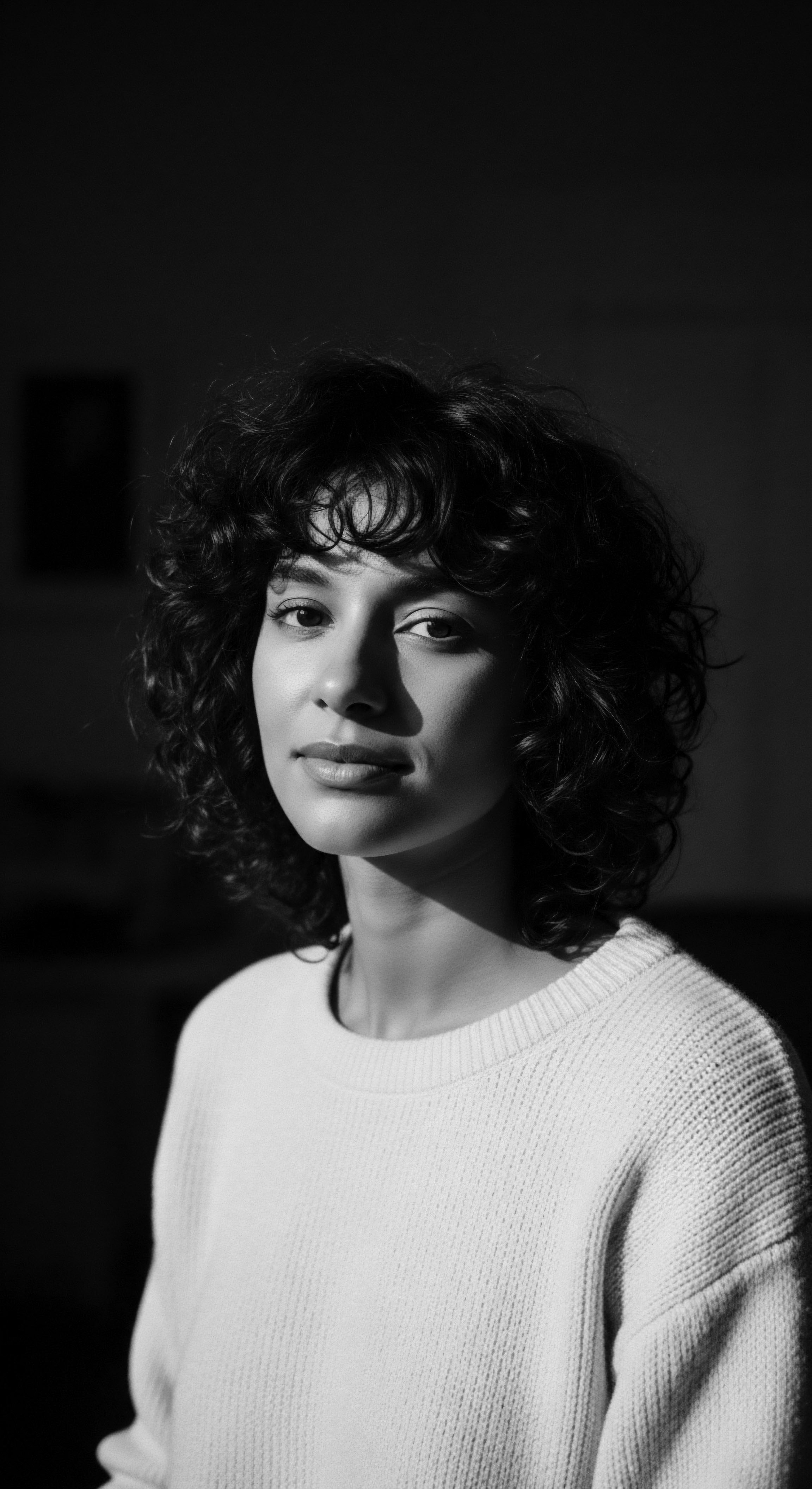 Portrait of a Woman with Naturally Coiled Hair in Dramatic Light This image is a celebration of natural coiled hair, emphasizing its beauty and inherent texture. Evoking a sense of cultural heritage, this monochrome portrait promotes acceptance and pride in diverse hair formations while highlighting the importance of holistic hair care practices.