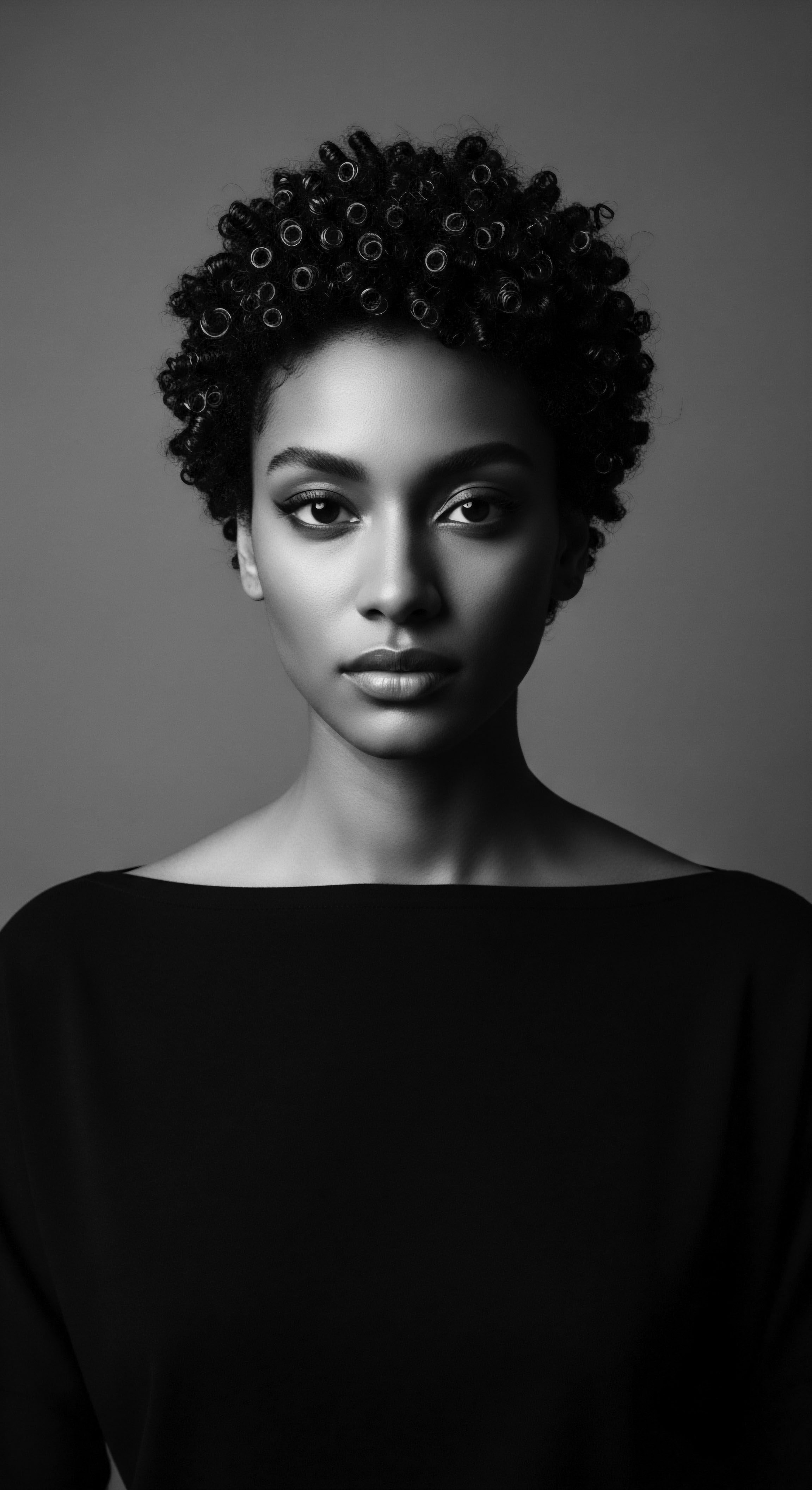 This artistic monochrome portrait exudes sophistication, portraying a woman with a meticulously styled short, coiled hairstyle that accentuates her features. The high contrast lighting draws attention to the hair's intricate texture and her refined expression, creating an image of inner strength and serene poise.