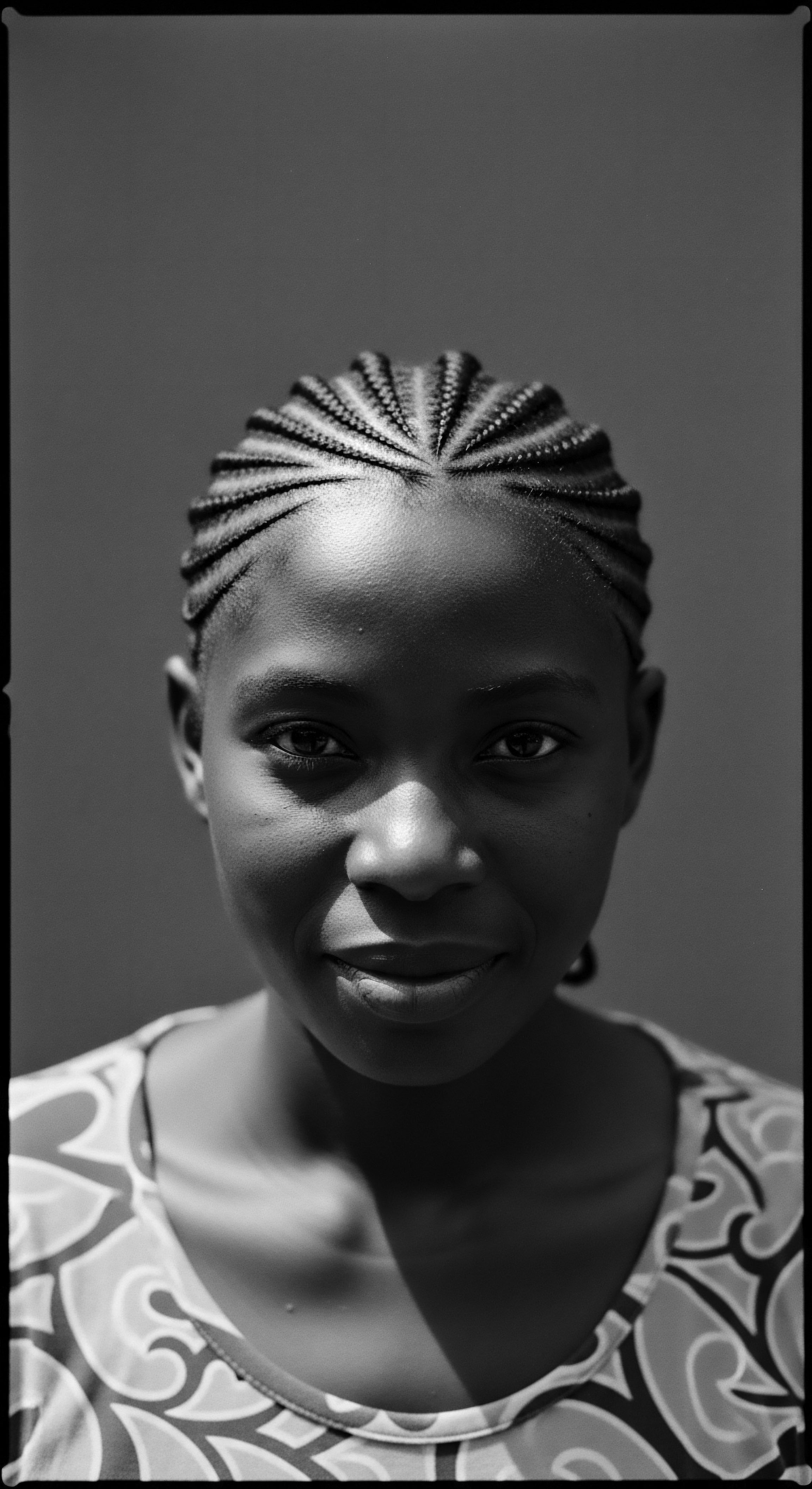 This portrait, rich in chiaroscuro, presents a young woman whose cornrow braid artistry speaks volumes about cultural heritage and self expression through meticulous coiffure, resonating with both timeless beauty and modern afrocentric identity, underscoring expert styling and technique.