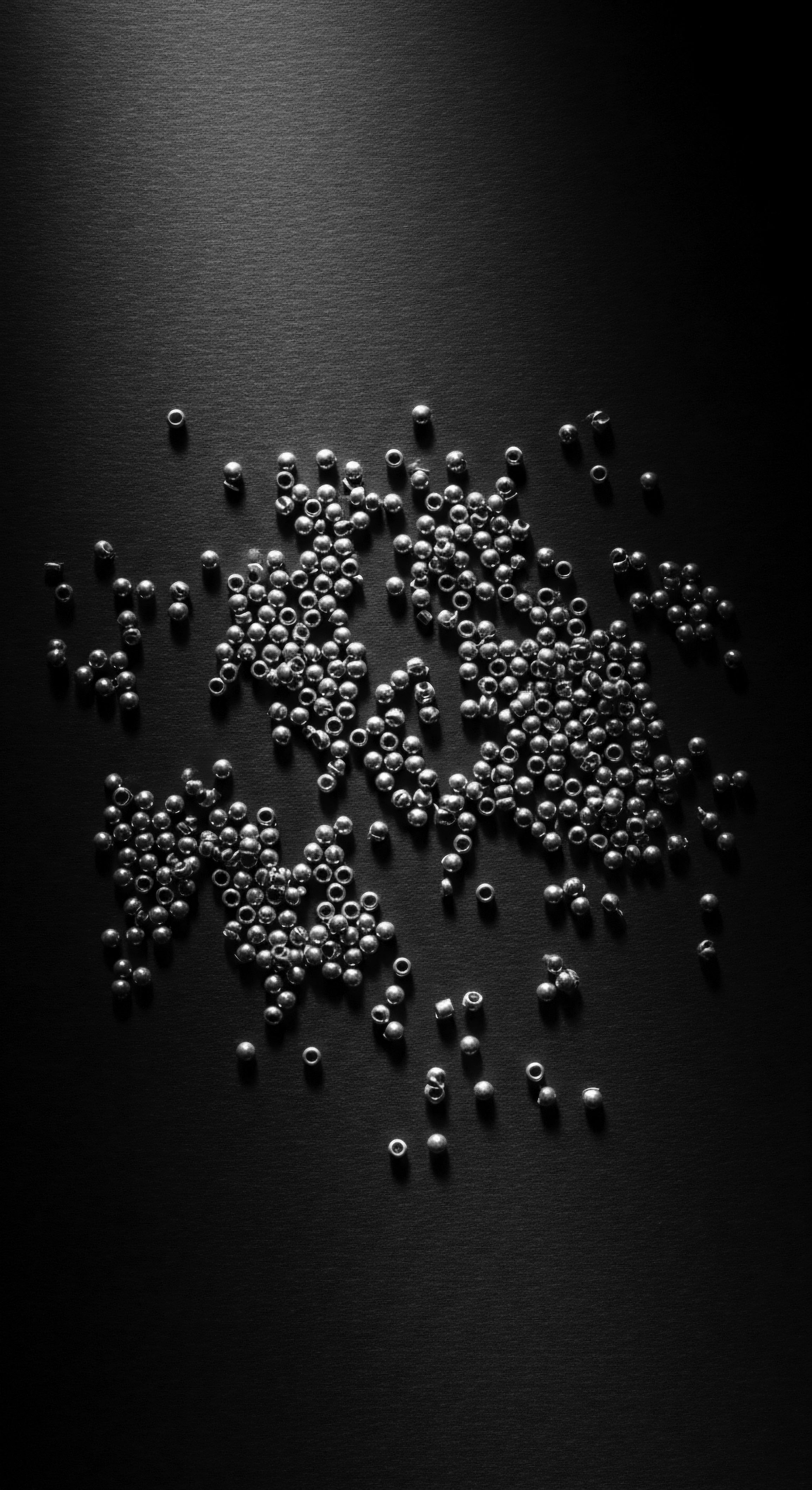 Silver Seed Beads on Black Background Textured Hair Ancestral Aesthetics The scattering of silver seed beads across the stark background presents a compelling visual metaphor for ancestral connections. Each bead mirrors a story within the expansive narrative of heritage and textured hair, reflecting traditions that honor wellness and expressive styling.