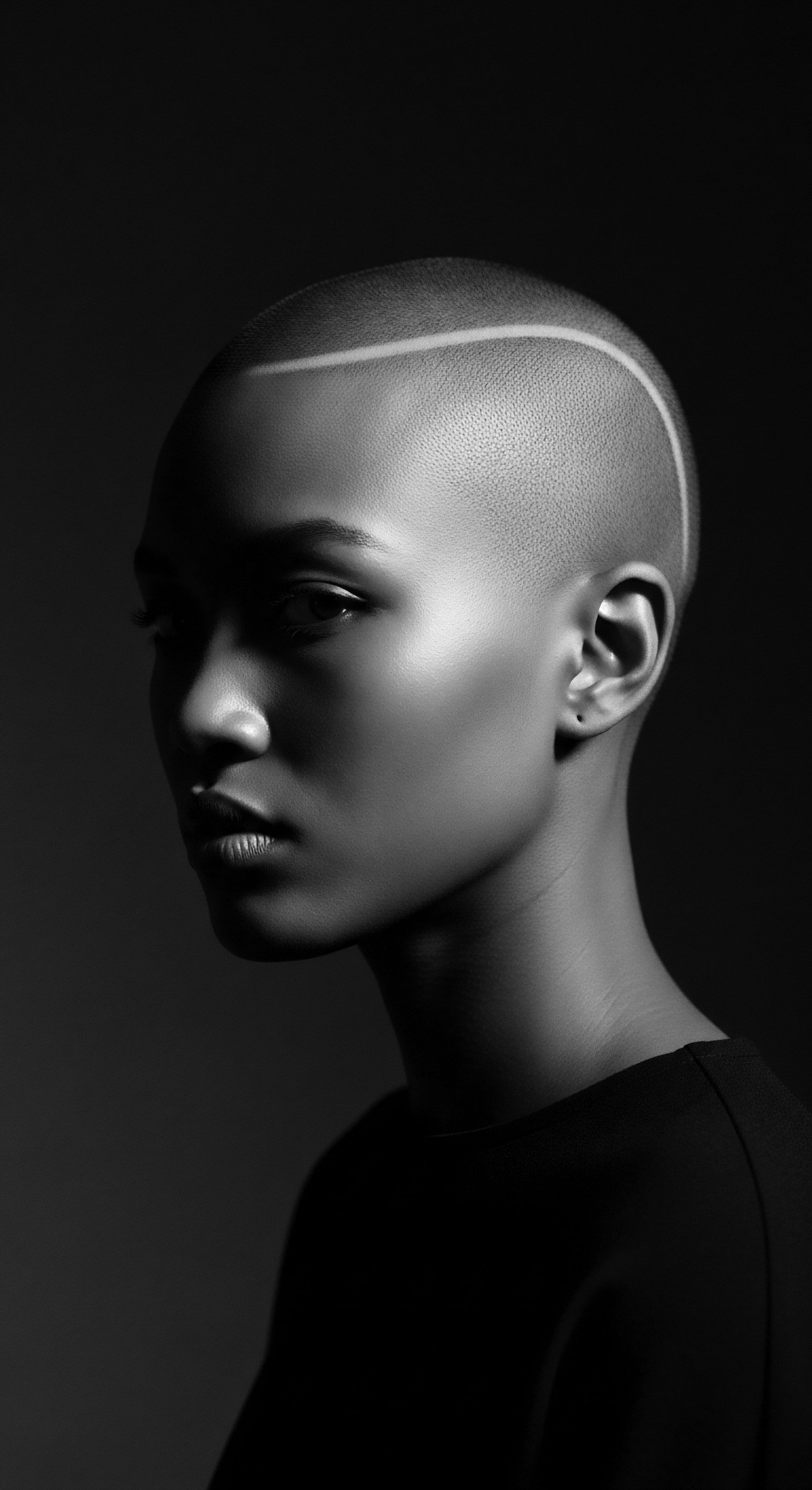 Striking Monochromatic Portrait of a Bald Black Woman with Skin Highlight The monochrome portrait features a Black woman with sleek lines, revealing both beauty and bold choices in personal presentation that honor skin and style, and embracing a contemporary aesthetic that complements her features, creating a strong visual statement about identity and self-expression.