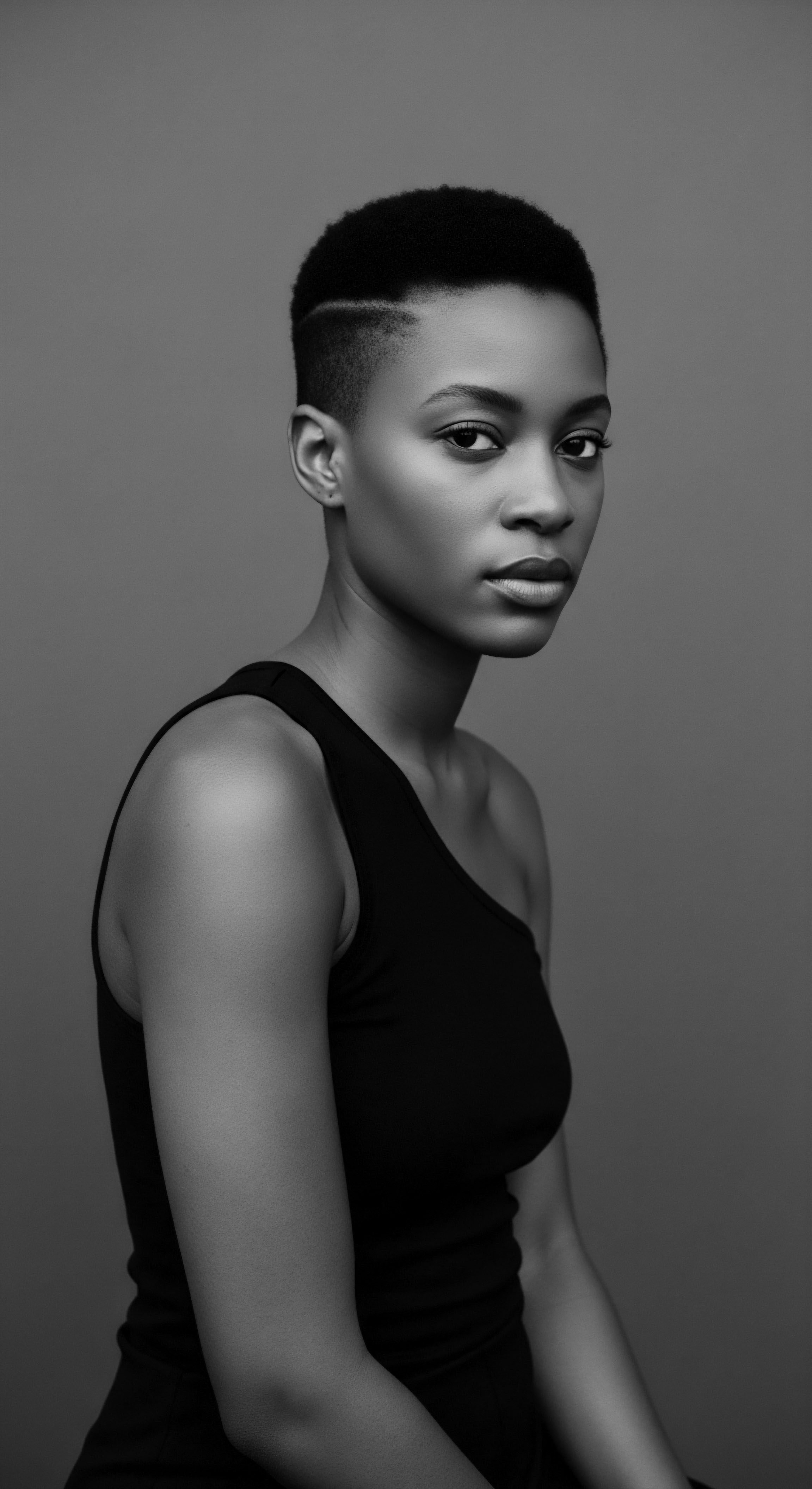 Striking Portrait of a Woman with Short Textured Hair and Fade The portrait evokes quiet strength and refined grace, reflecting modern black hair expression through carefully sculpted coils and fades that complement facial aesthetics. This image invites consideration of textured hair's role in self expression and cultural identity, showcasing versatility and empowerment.