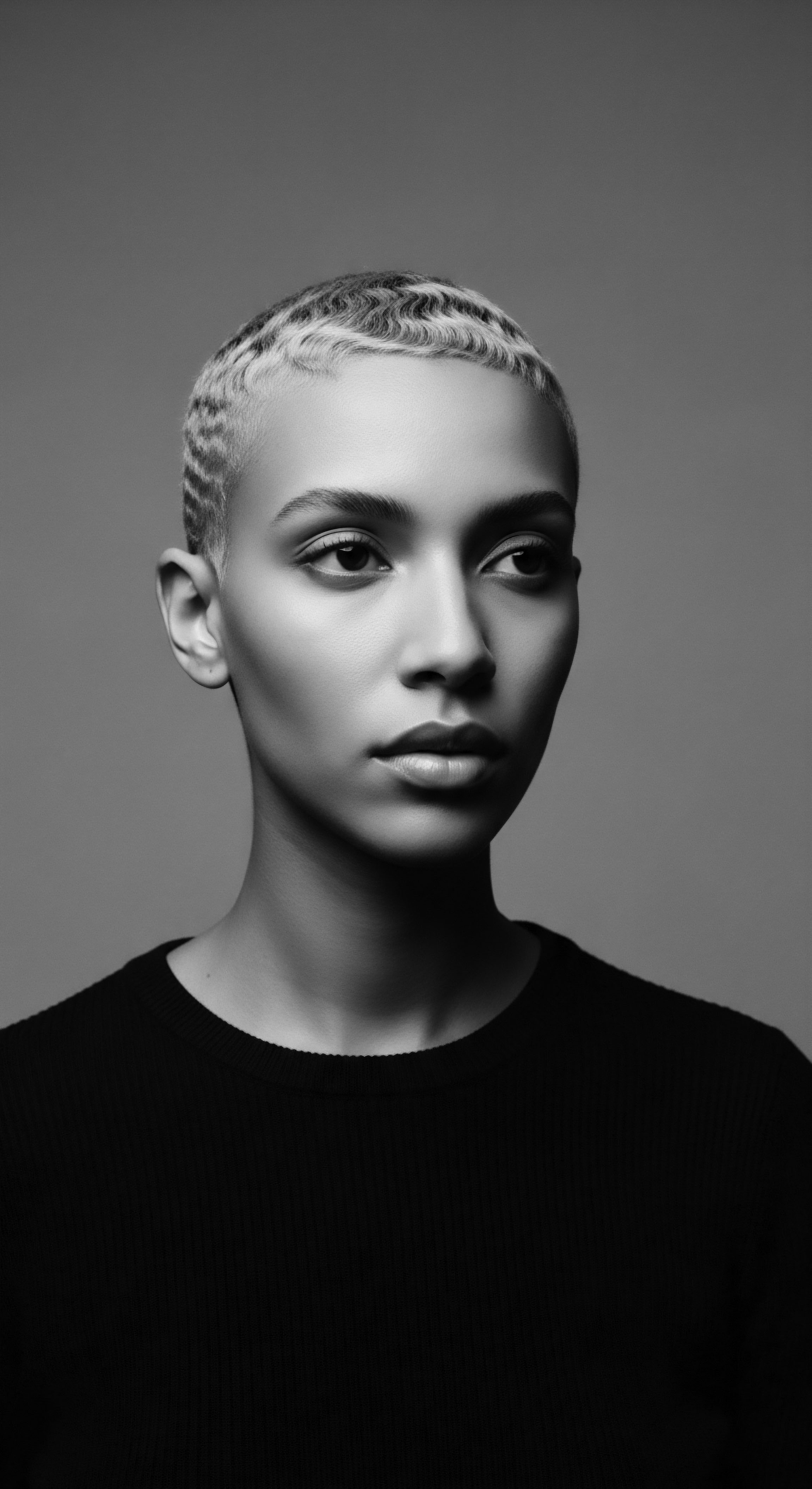 This evocative portrait captures the essence of modern beauty through short, textured hair, the monochrome palette emphasizing the sculpted waves and clean lines, offering a contemporary take on a classic style that speaks to individuality, confident self-expression and embracing of natural texture.
