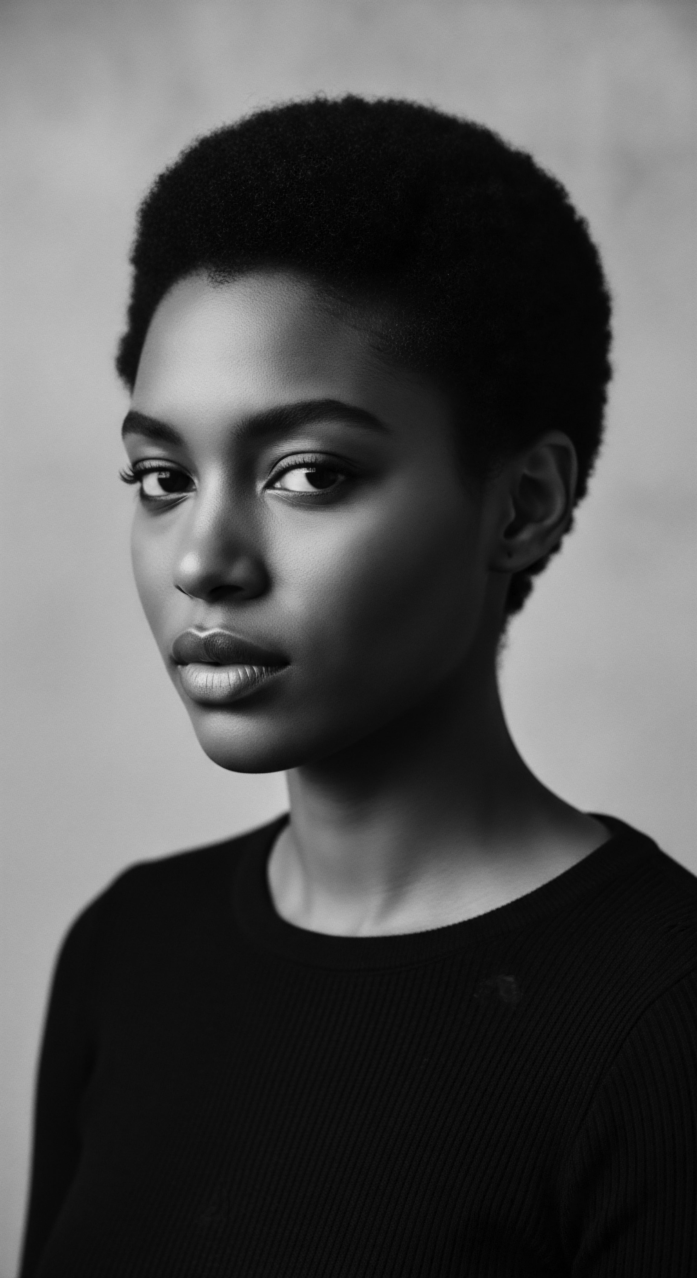 The striking monochrome portrait captures the essence of Black womanhood, her natural short cropped afro hairstyle symbolizing strength and cultural pride. Evoking ancestral heritage and expressive beauty, she embodies a timeless elegance, with her gaze conveying a sense of self-assuredness and resilience.