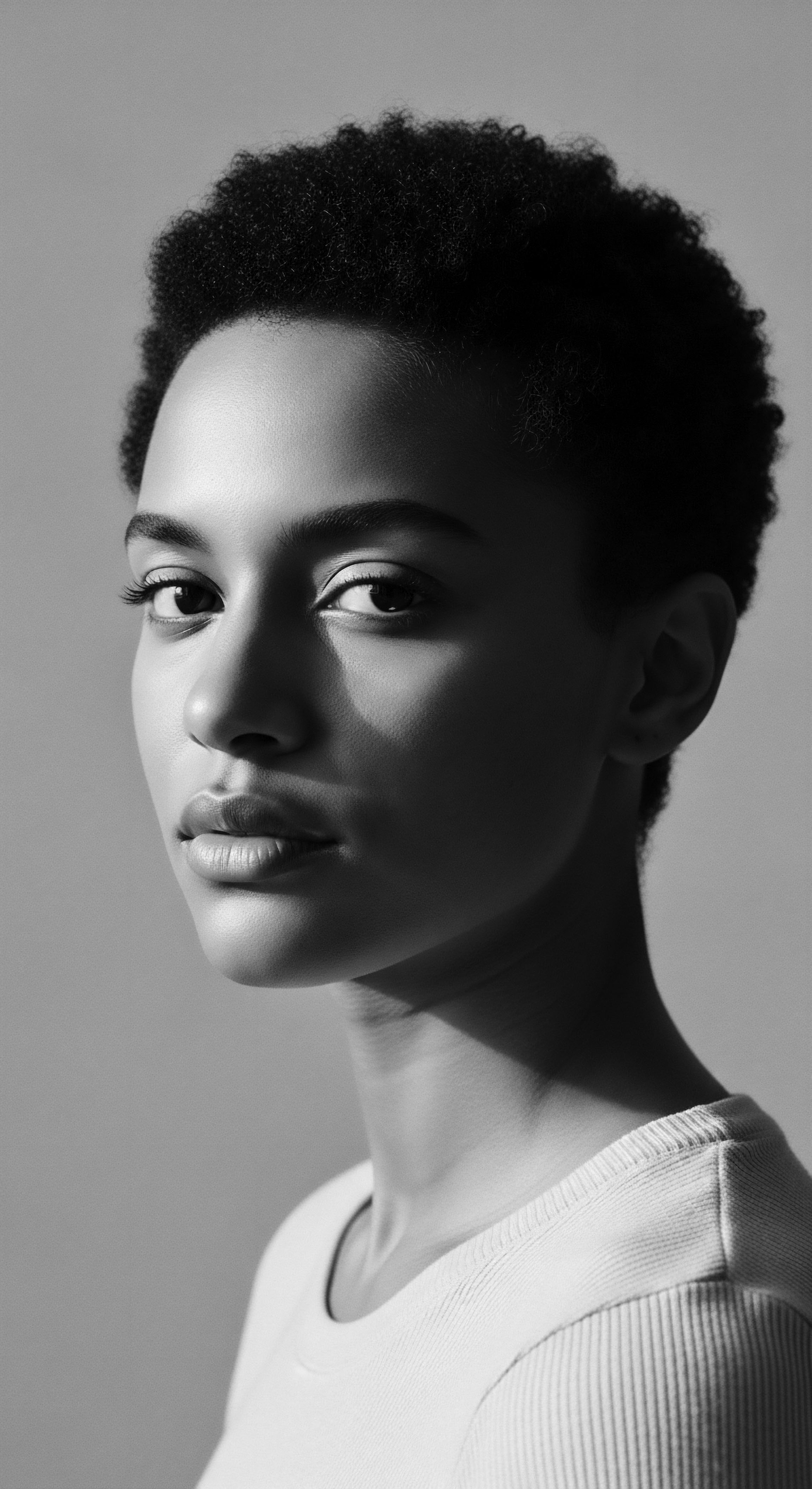 Striking Portrait of Young Woman with Natural Afro Textured Hair The black and white portrait evokes timeless elegance as the model's natural afro textured hair becomes a statement of heritage. This visual narrative promotes diversity, showcases natural Black hair aesthetics, and celebrates the beauty of Black women and textured hair expression.