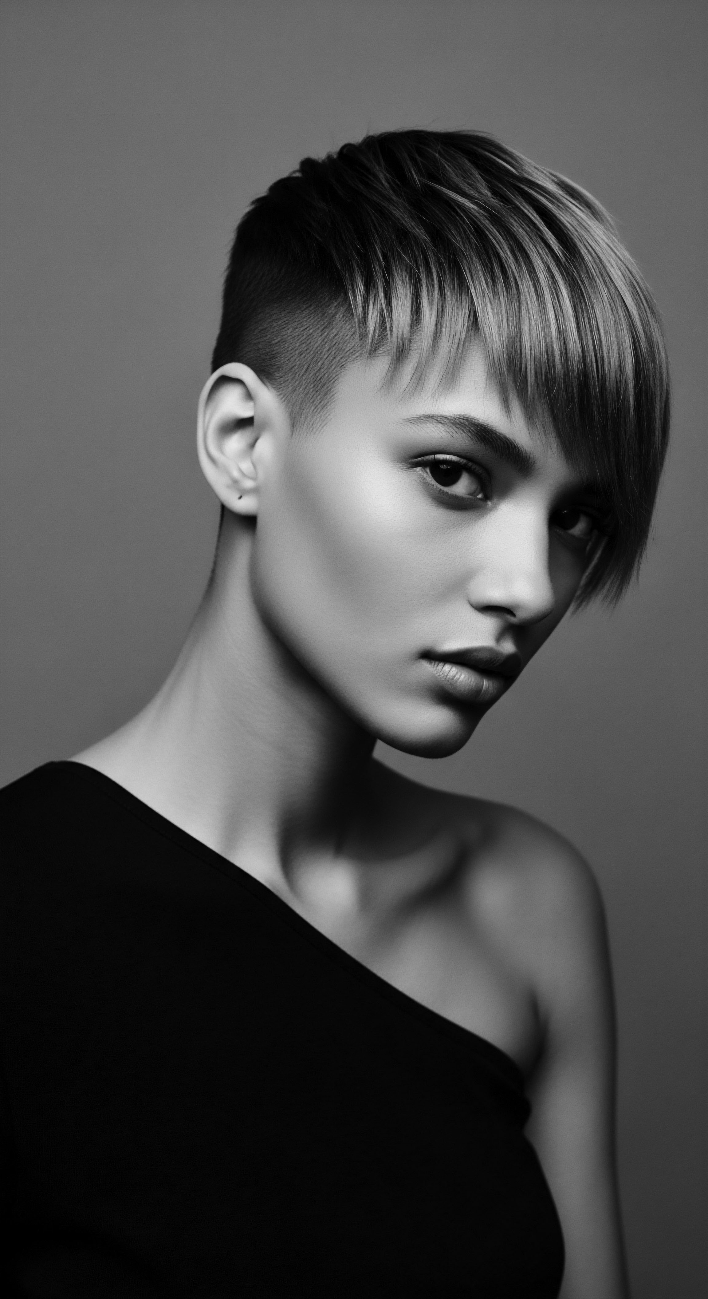 Striking Portrait Undercut Hairstyle Expressive Stare Textured Fringe in Monochrome Study The interplay of light and shadow accentuates the angular planes of the face, focusing on the subject's intense gaze. Undercut textured hairstyle is an embodiment of individuality. The textural contrasts underscores a modern ethos of expressive styling and boldness.
