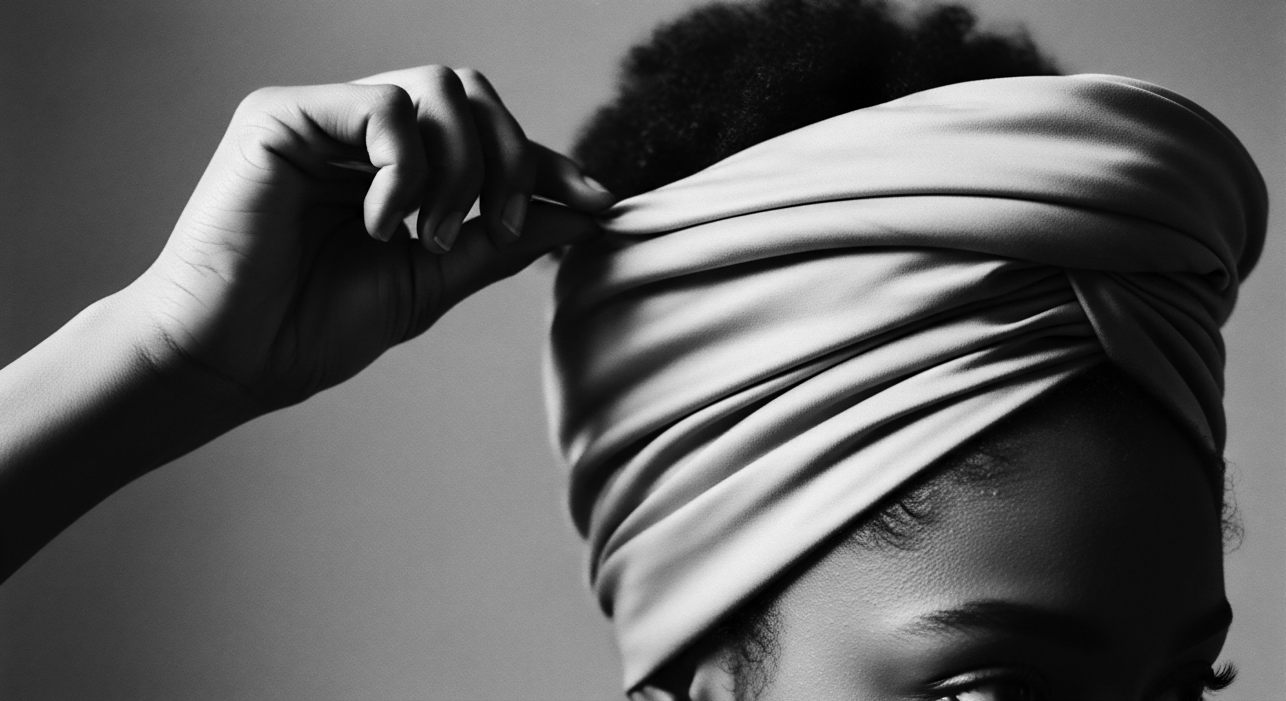 Woman Adjusting Silk Turban Protective Style for Natural Hair Care The image captures the deliberate act of adjusting a silk turban, reflecting protective styling's commitment to hair health, celebrating natural textures and the historical significance of headwraps within Black communities, emphasizing moisture preservation and promoting healthy hair growth through cultural haircare practices.