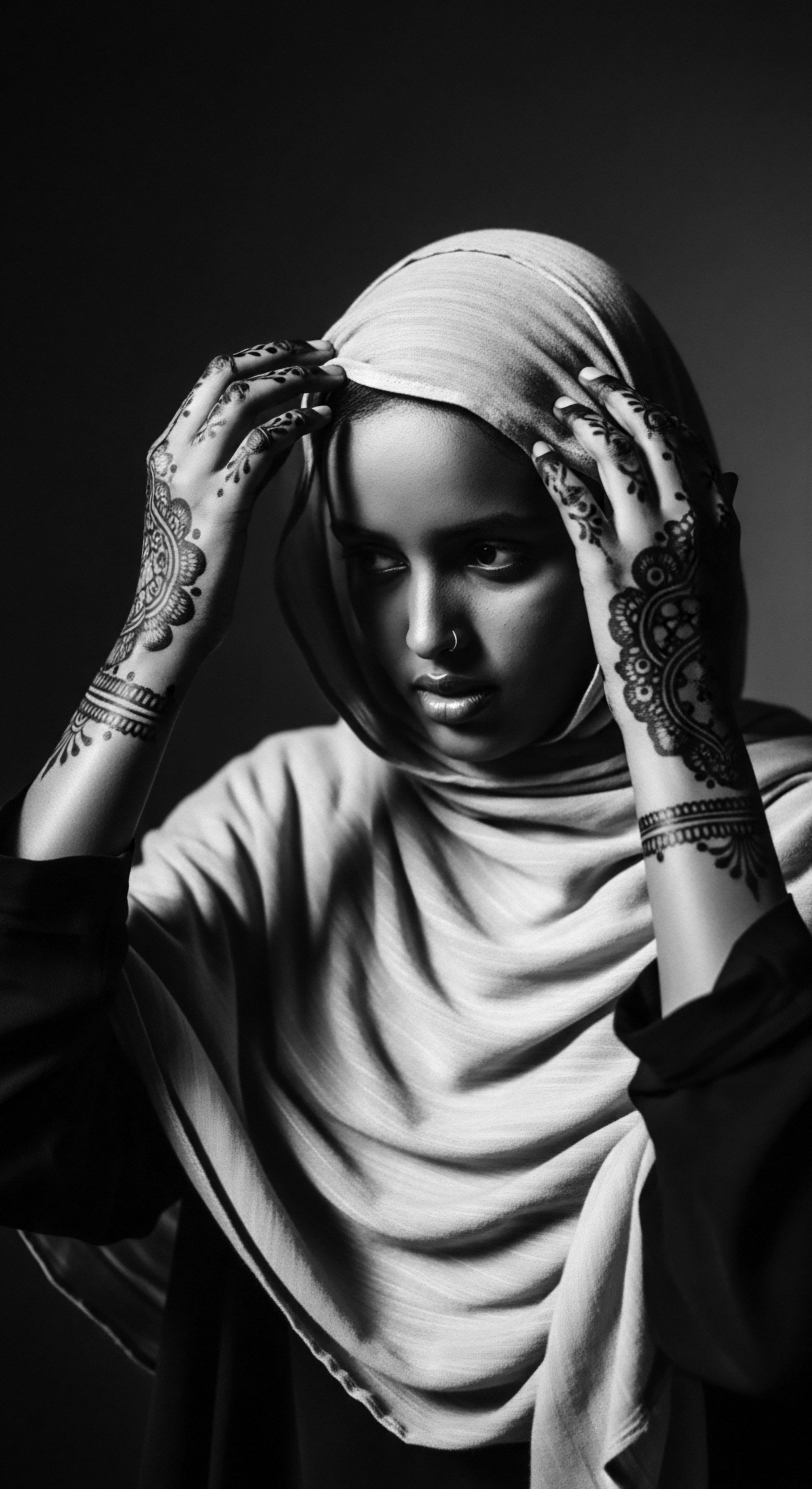 Woman in Hijab with Henna Hands Spiritual Portrait Black and White This evocative portrait captures a woman's strength and serenity, expressed through the harmony of henna designs and the soft folds of her hijab, symbolizing both cultural pride and a graceful intersection of self-expression and the timeless narratives of ancestry.