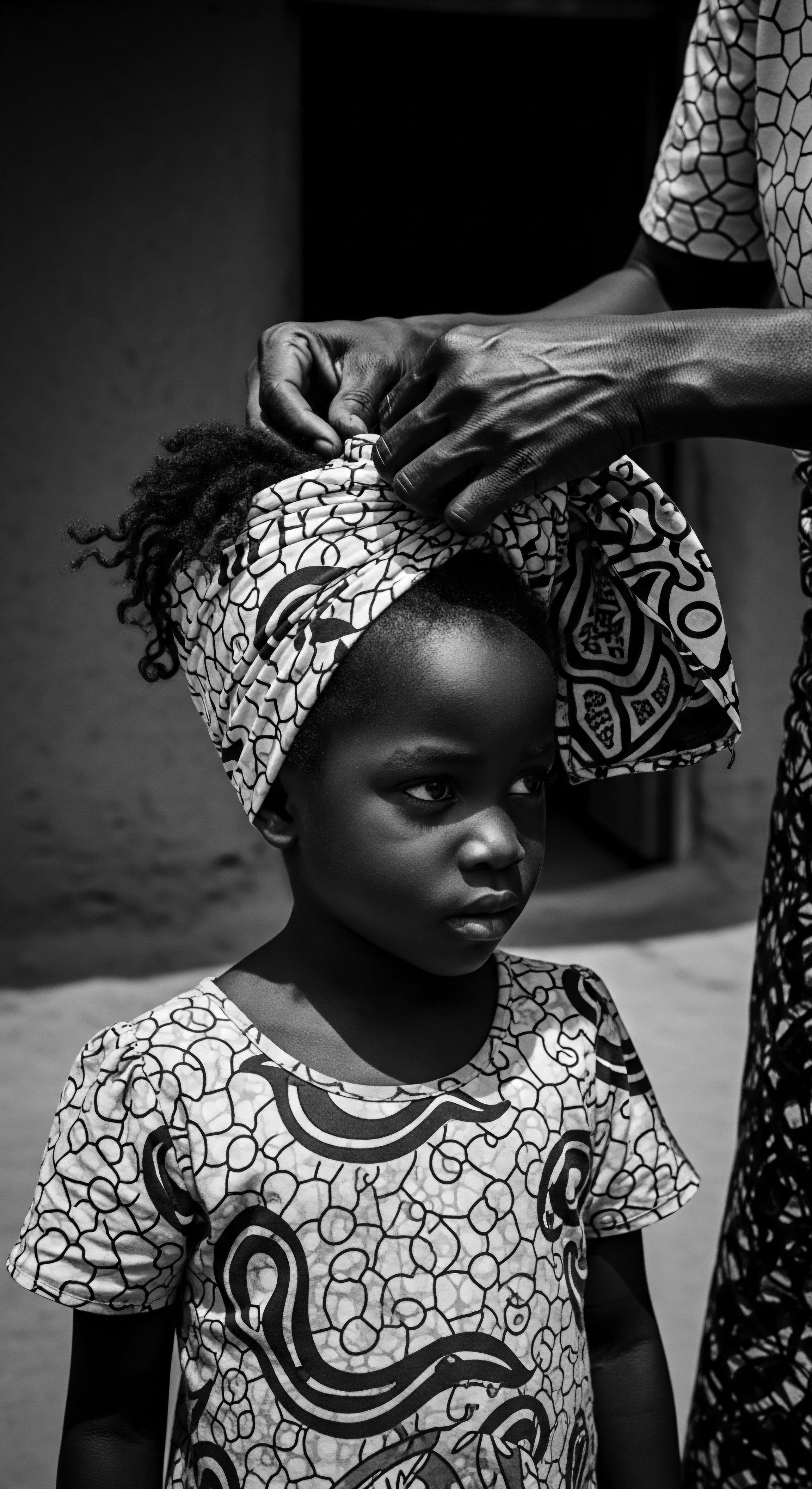 Young Girl Receiving Traditional Headwrap A Black and White Portrait The delicate placement of a patterned headwrap upon the girl, shows intergenerational care, and respect for Black hair traditions and beauty standards. This visual conveys ancestral strength, and the beauty of cultural heritage, and the importance of shared wellness practices passed down through generations, defining identity.