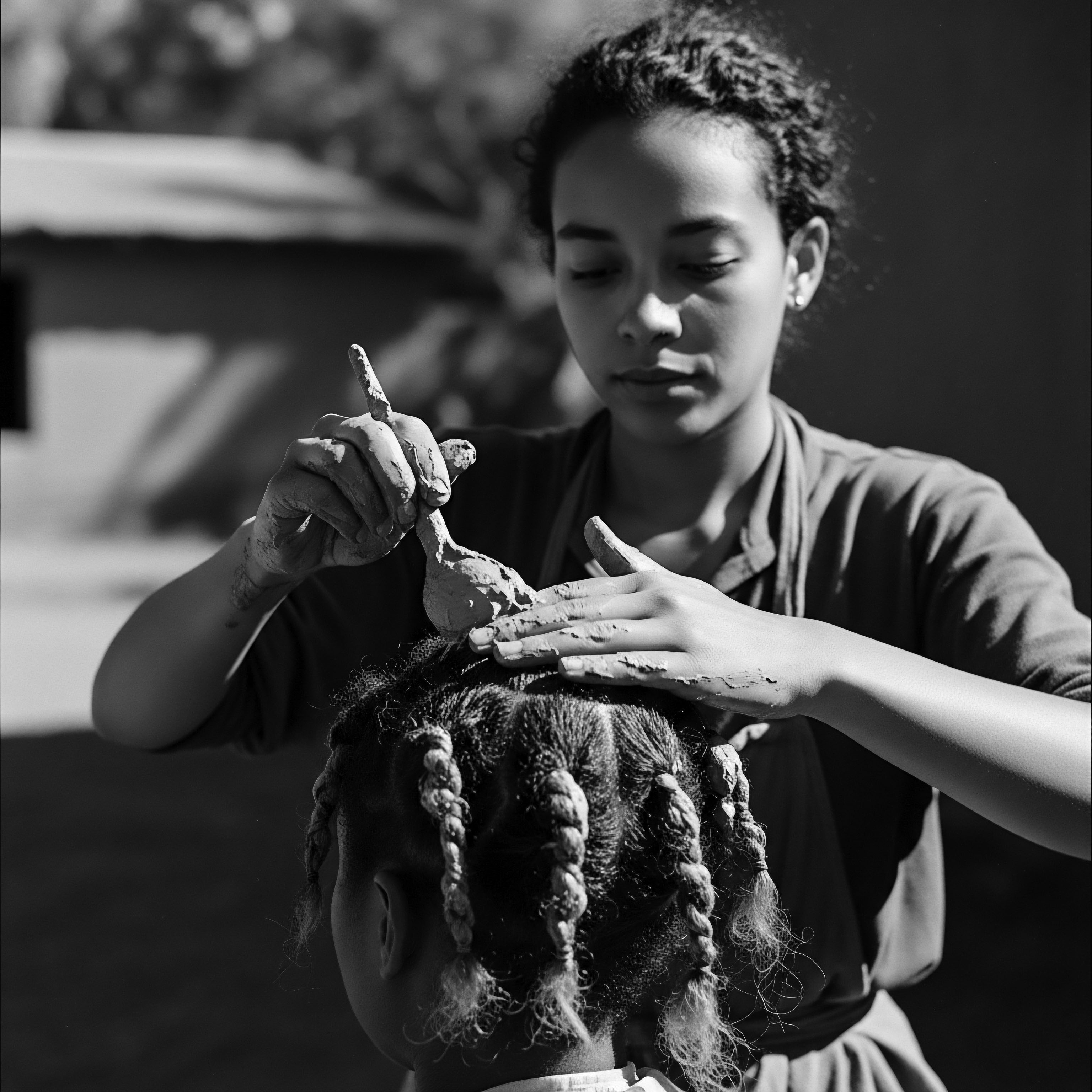 Young Woman Applies Clay Hair Mask to Child’s Braided Spirals The timeless image captures a tender moment of hair care, blending traditional methods with a holistic approach. Nutrient-rich clay nourishes the child's scalp, celebrating an ancestral practice of textured hair wellness and the bond between generations, promoting healthy growth and honoring Black hair traditions.