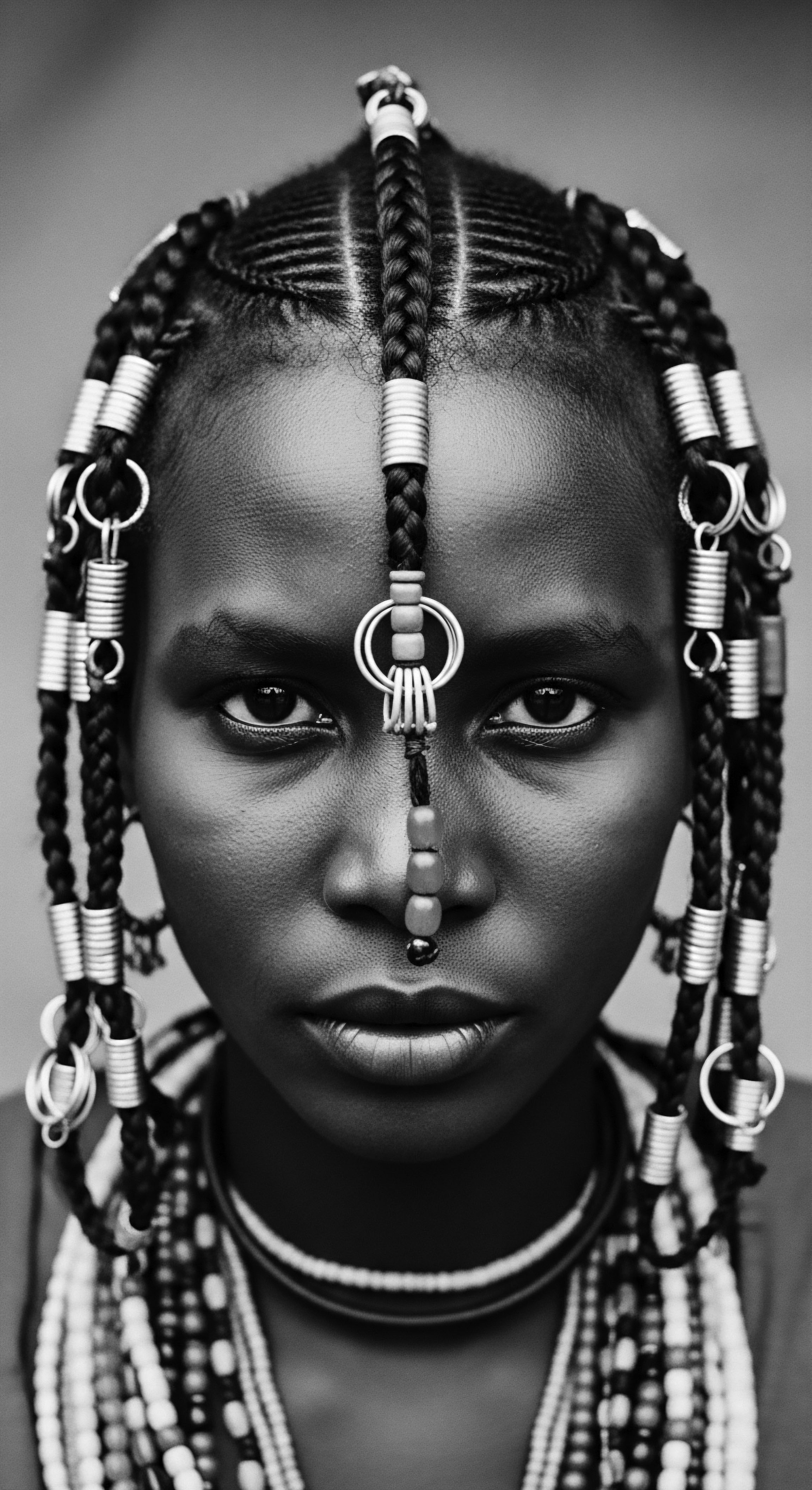 Young Woman Displaying Braided Hairstyle with Embellishments Cultural Pride and Heritage The serene gaze of this young person, combined with intricate coil work and culturally significant hair ornaments, powerfully communicates resilience and pride. This artistic representation celebrates textured hair forms, a legacy preserved through braiding practices, while embracing holistic beauty and a commitment to ancestral heritage.